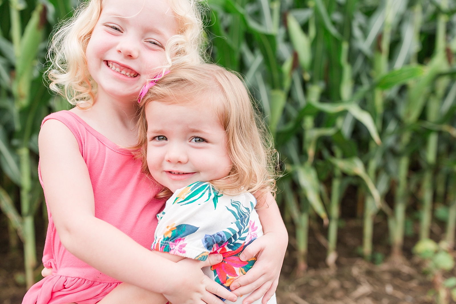 sisters hugging and smiling at the camera in a cornfield barefoot photo