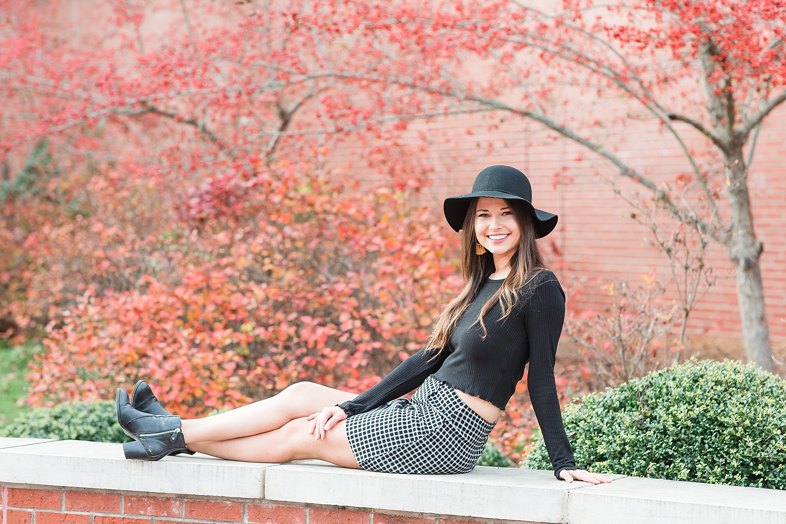Western Carolina University Senior Sierra sitting on brick wall in front of red trees smiling at camera Photo