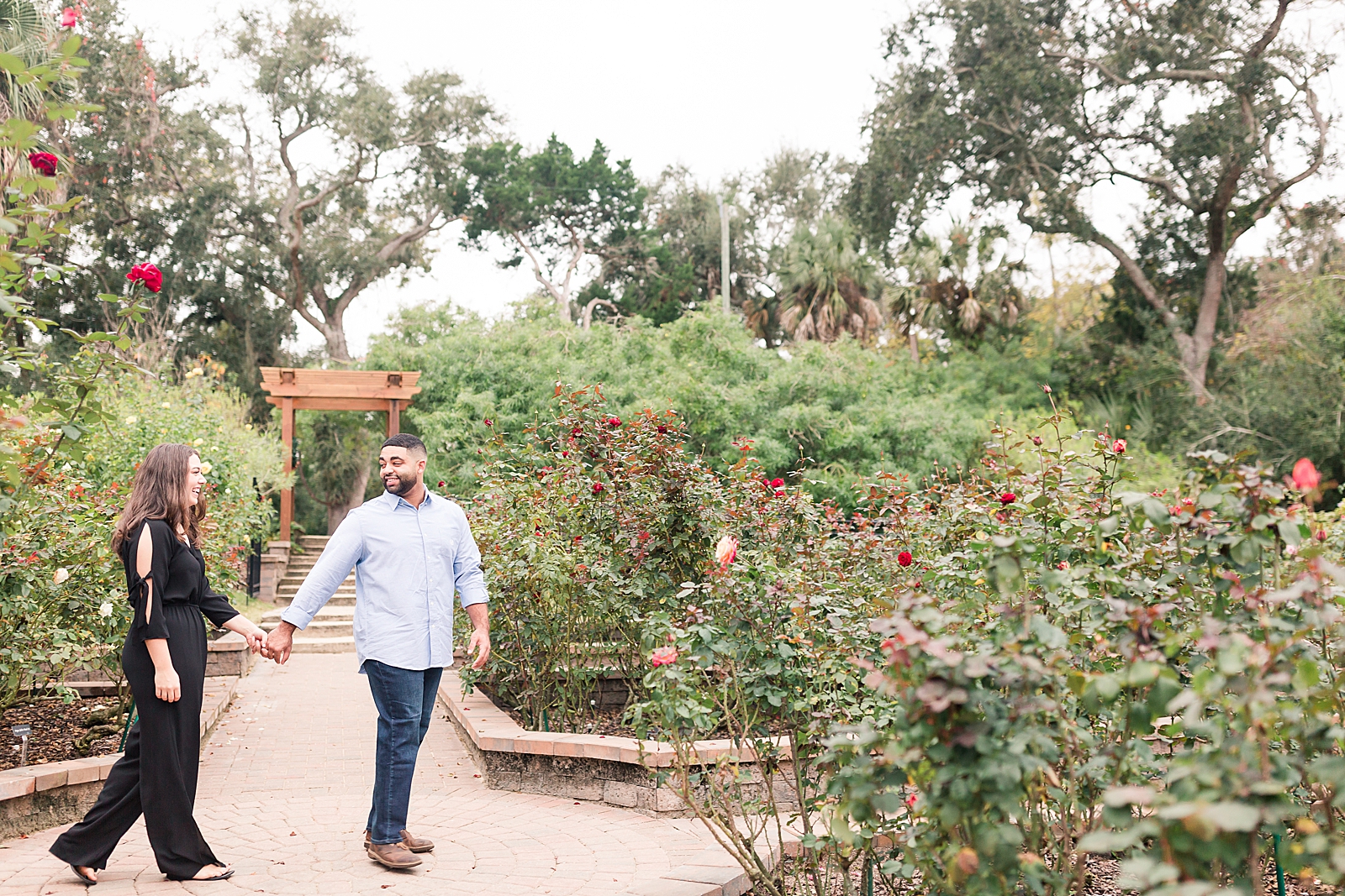 St. Augustine Engagement Nick and Chloe holding hands walking through rose garden Photo