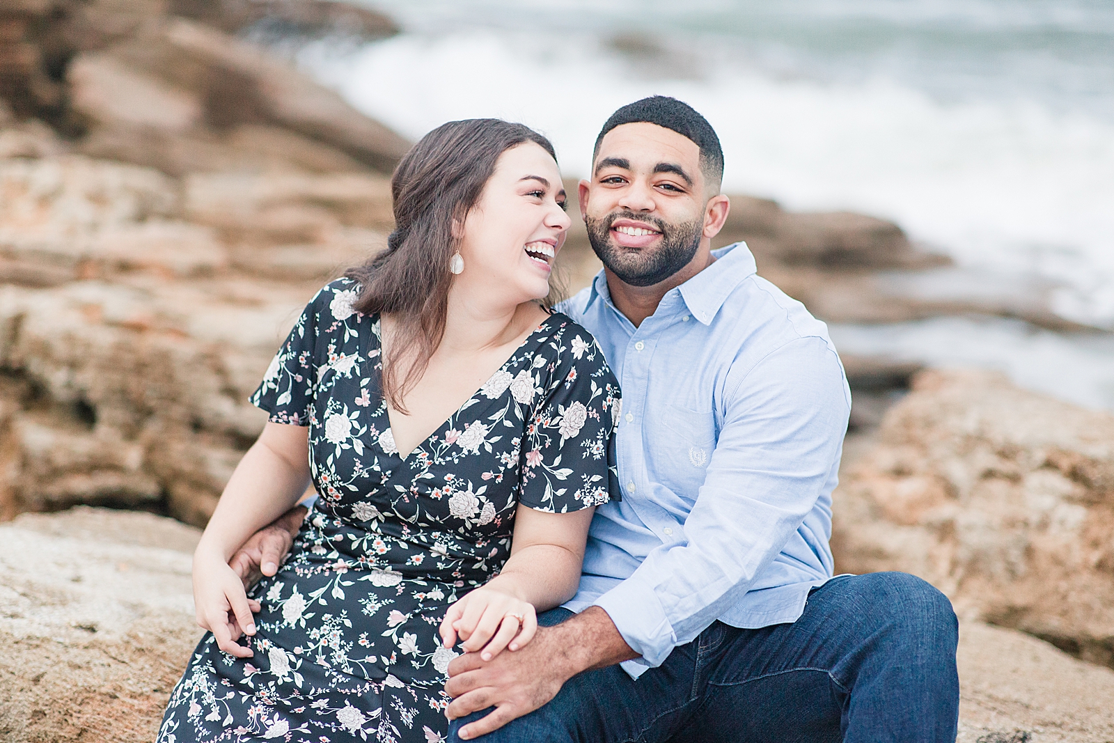 St. Augustine Engagement Couple sitting on rocks and laughing at each other at the beach Photo