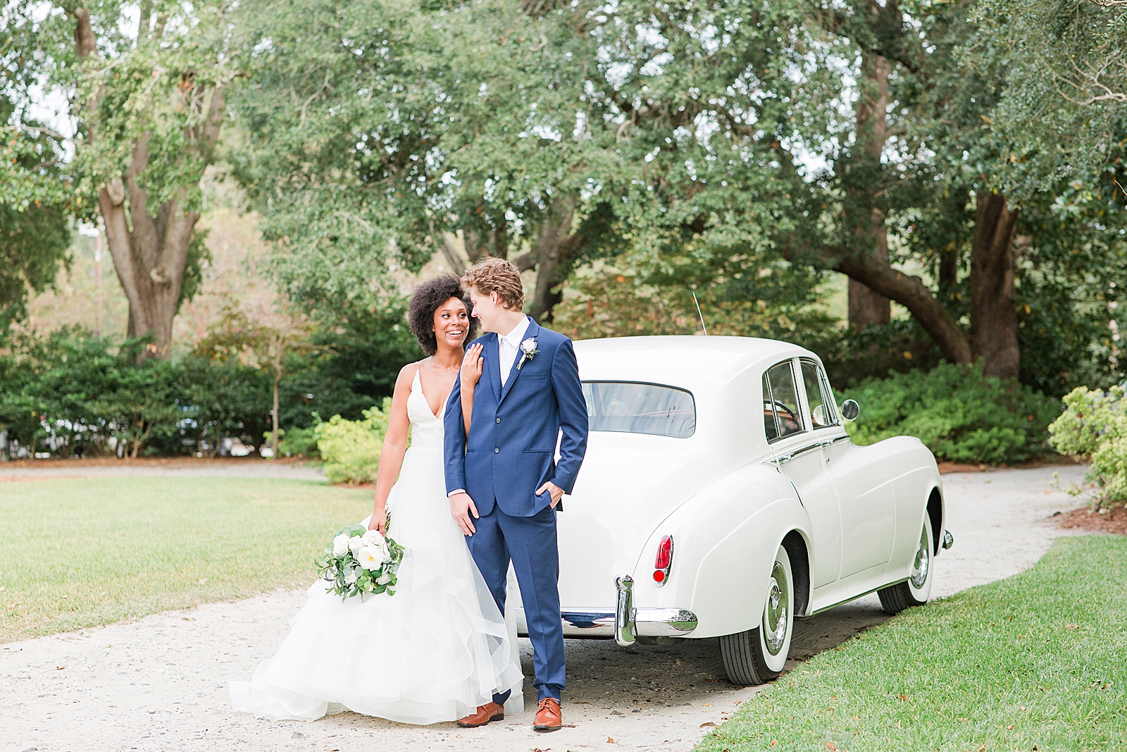 Lowndes Grove Wedding Bride and Groom in smiling at each other in front of a vintage white car Photo