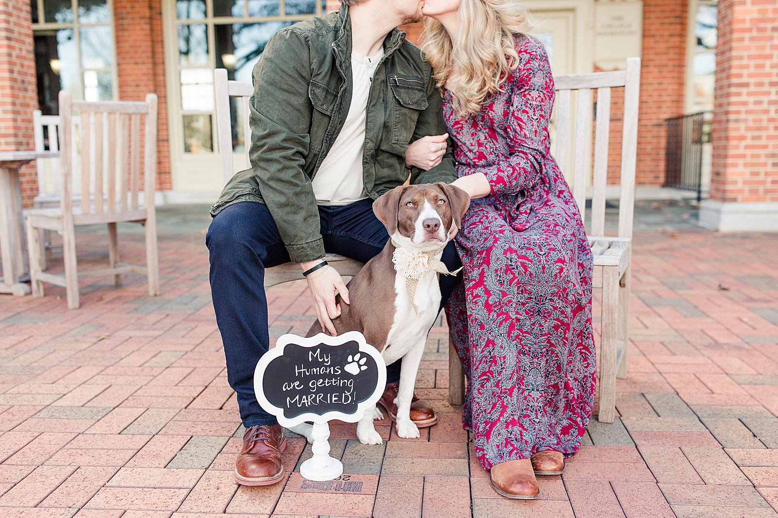 Winston-Salem Engagement Session Couple kissing with dog in front and sign that says my humans are getting married Photo