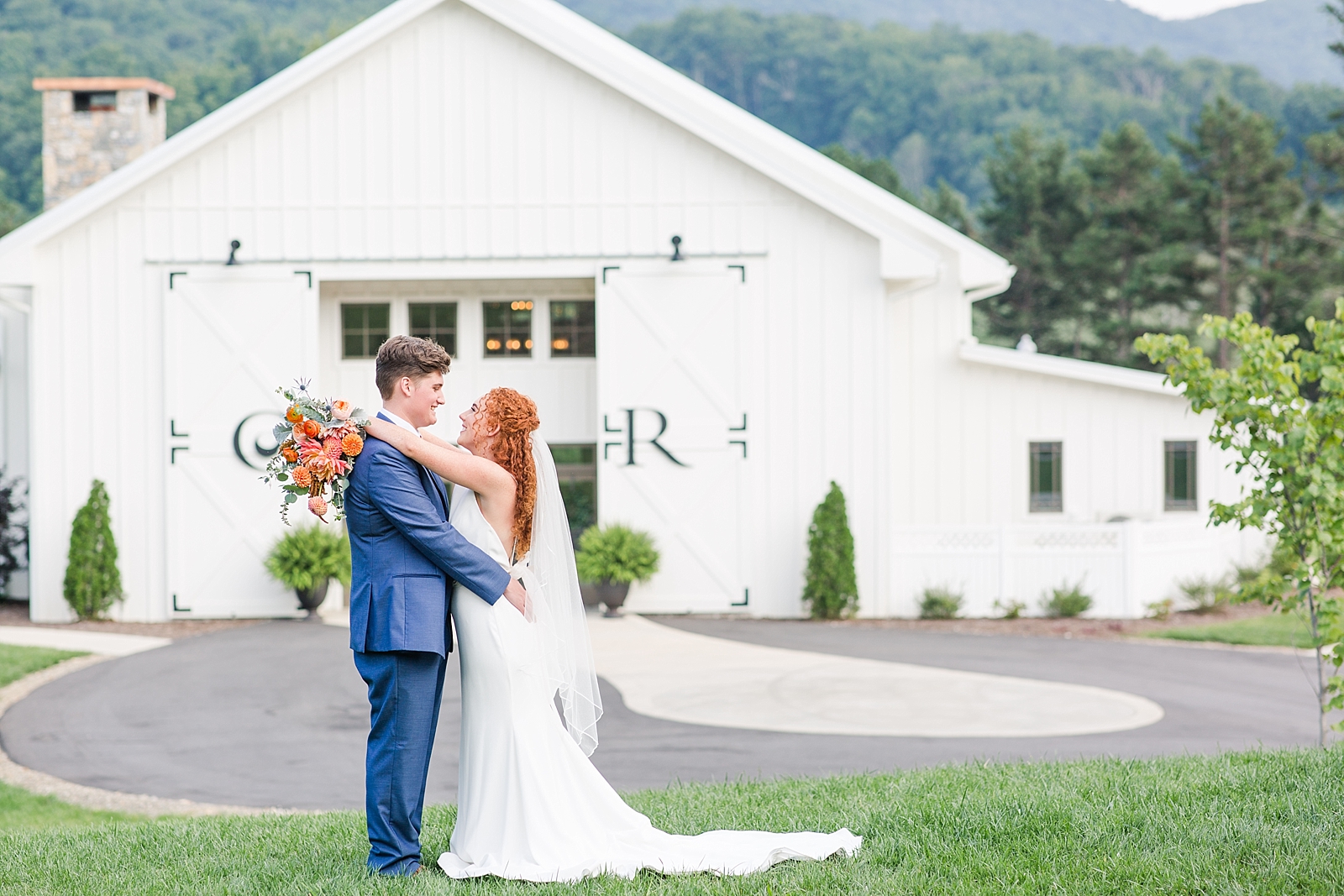 Chestnut Ridge Wedding bride and groom hugging with bouquet over grooms shoulder in front of white barn Photo