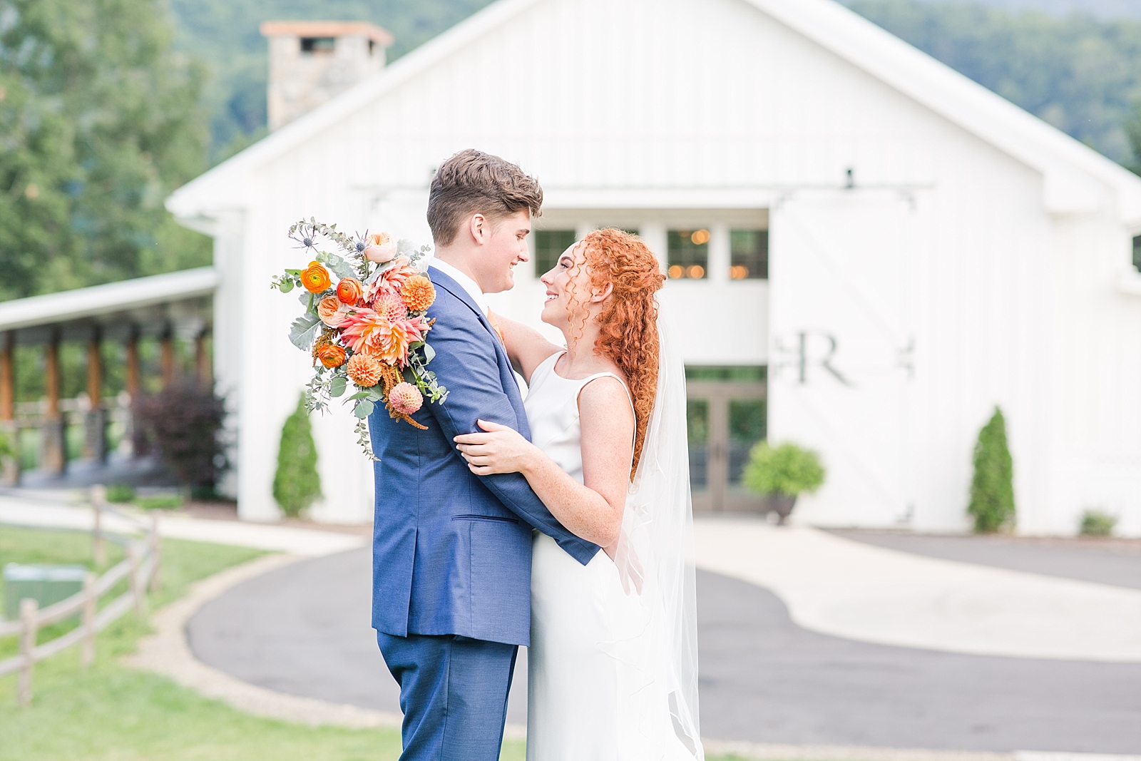 Chestnut Ridge Wedding bride and groom smiling at each other in front of white barn Photo