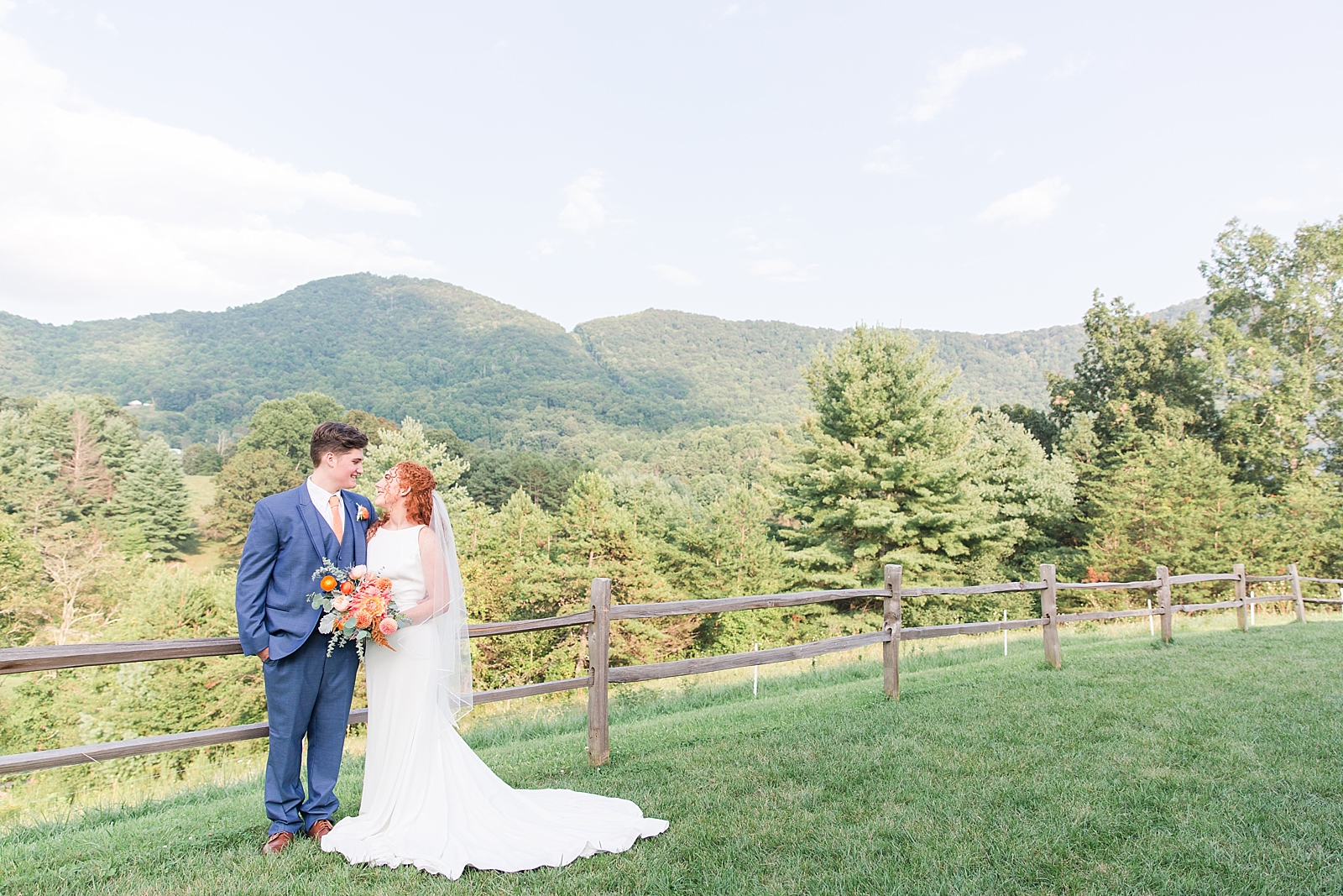 Chestnut Ridge Wedding bride and groom smiling at each other leaning on split rail fence with mountain background Photo