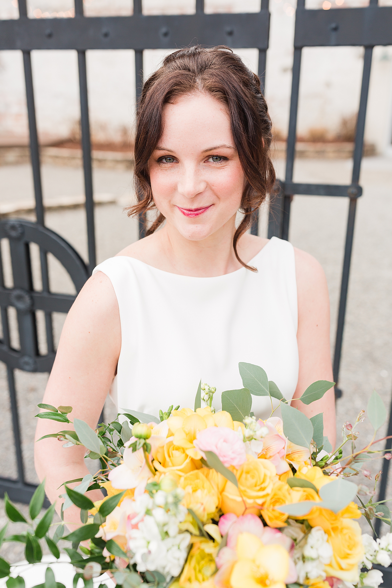 Hackney Warehouse Spring Bridal Session Bride Grinning in front of iron gates with yellow bouquet Photo