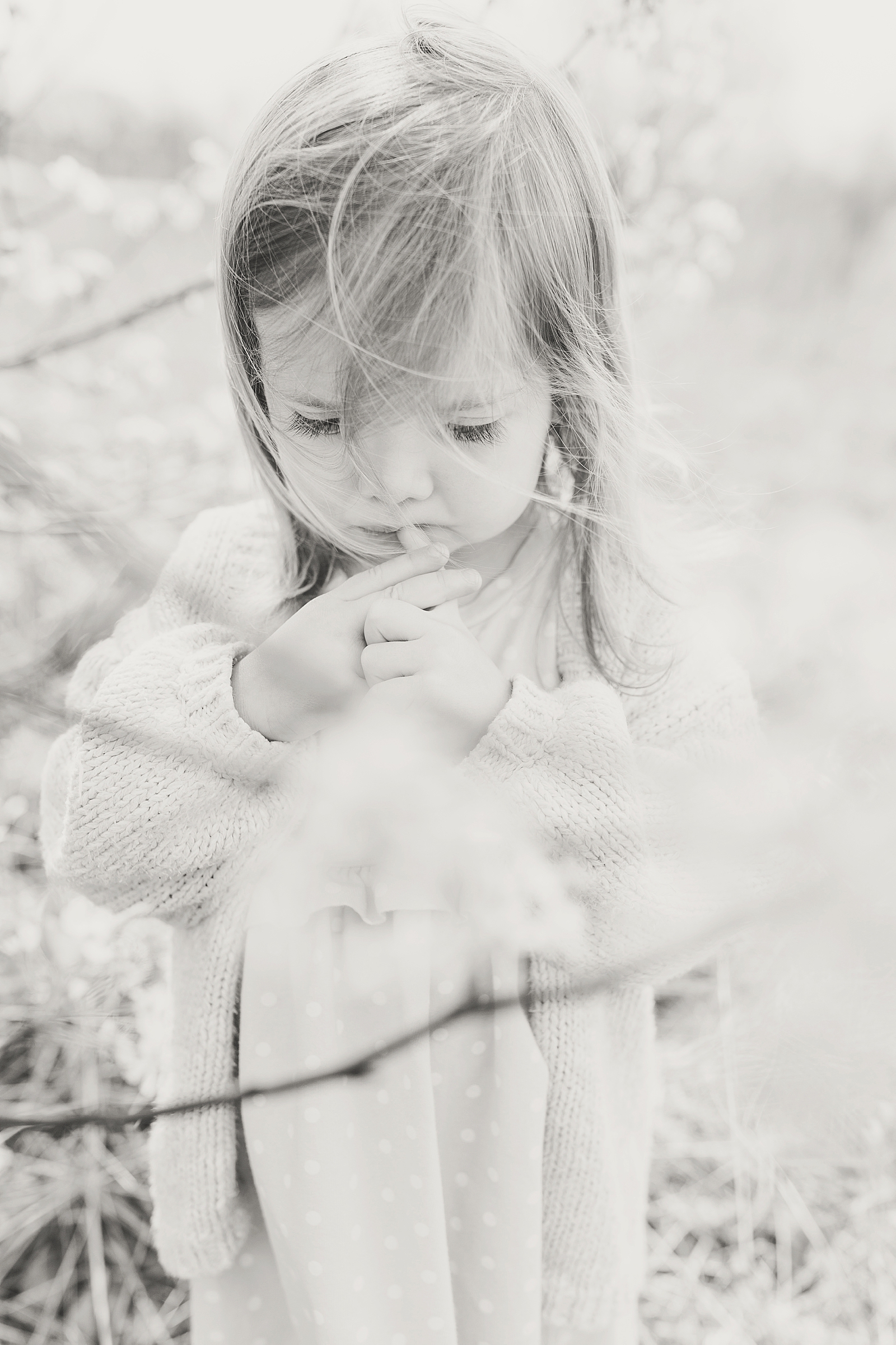 Asheville Photographer's Family Black and White of little girl in tree branches looking down with finger at lips concerned Photo