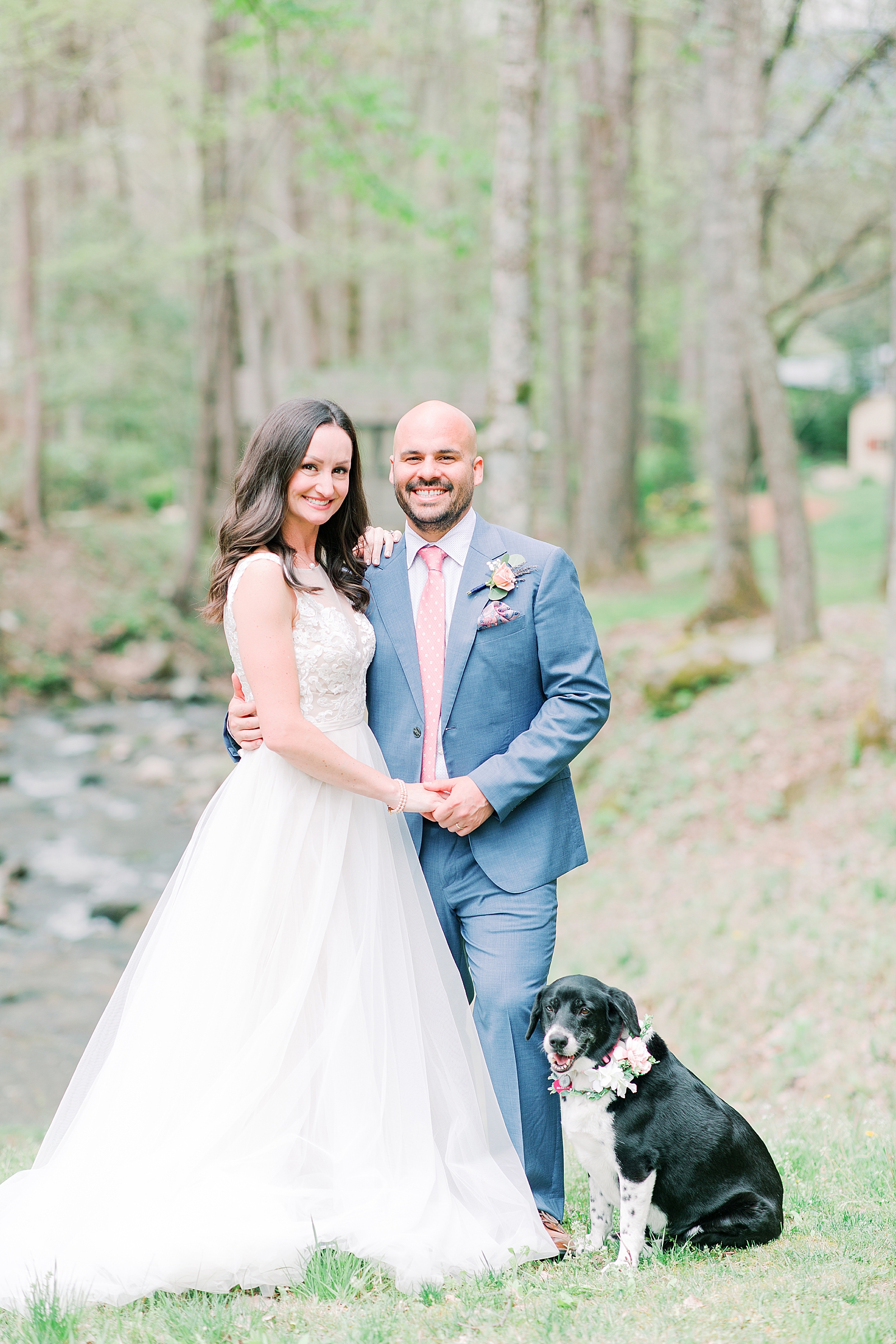 Spring Hawkesdene Wedding Bride and Groom smiling at camera holding hands with dog in front of creek Photo