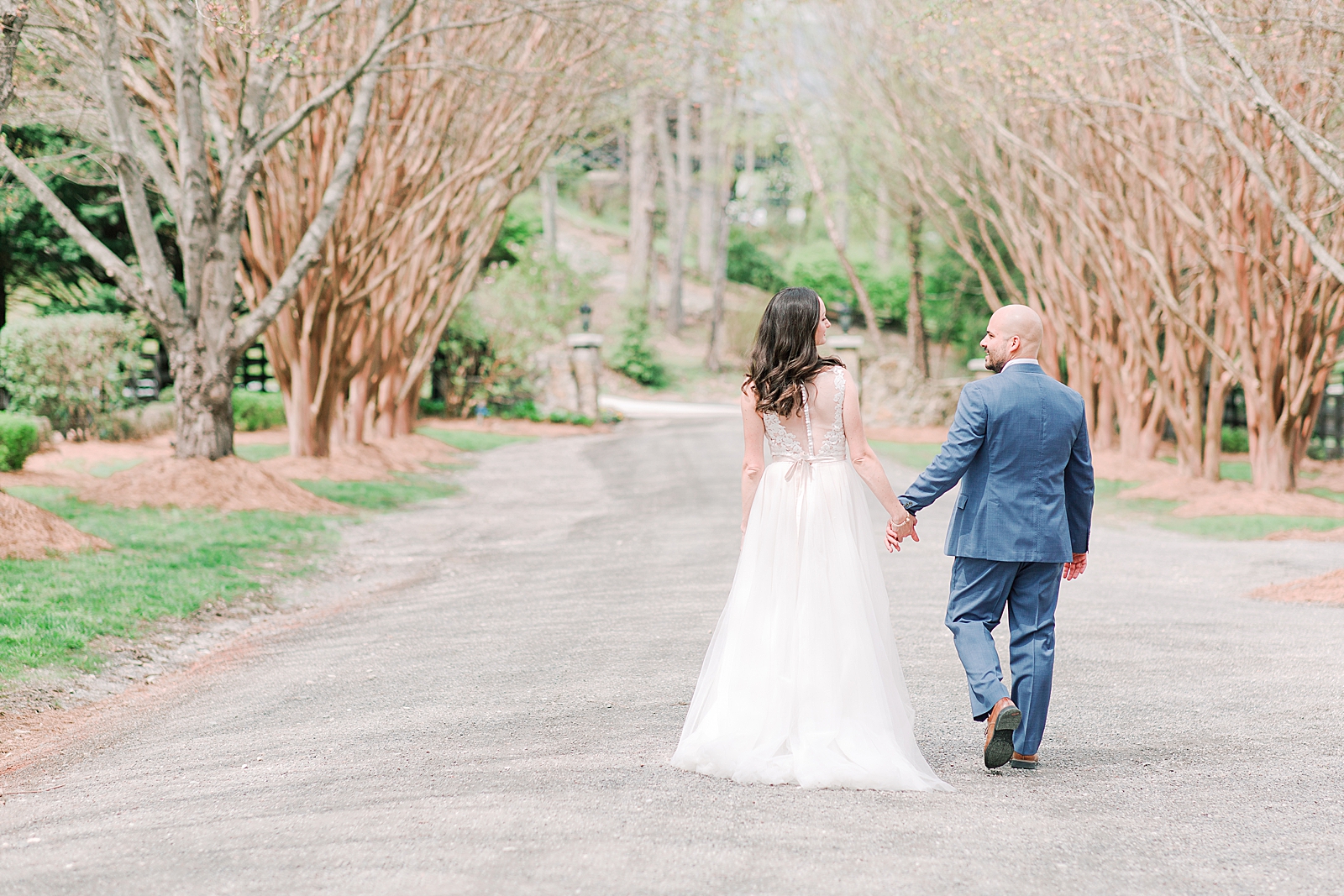 Spring Hawkesdene Wedding Bride and Groom holding hands walking down tree lined driveway Photo