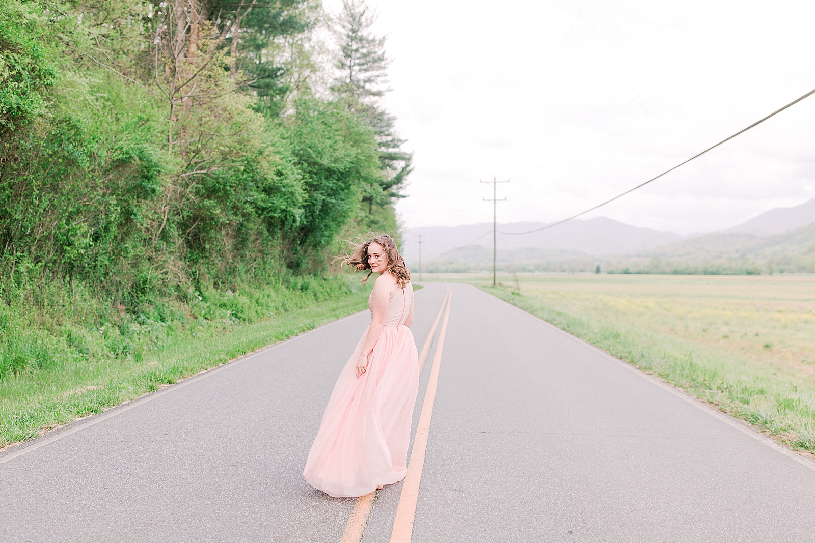 High School Senior Session Girl in Pink Prom Dress walking down road looking over her shoulder Photo