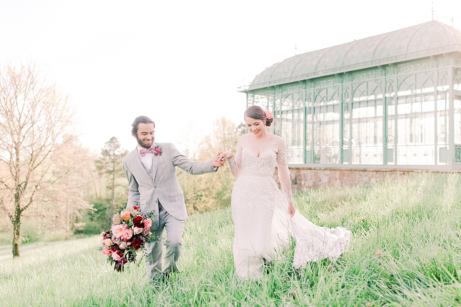 2400 On The River Wedding Bride and Groom walking through grass holding hands in front of Greenhouse Photo