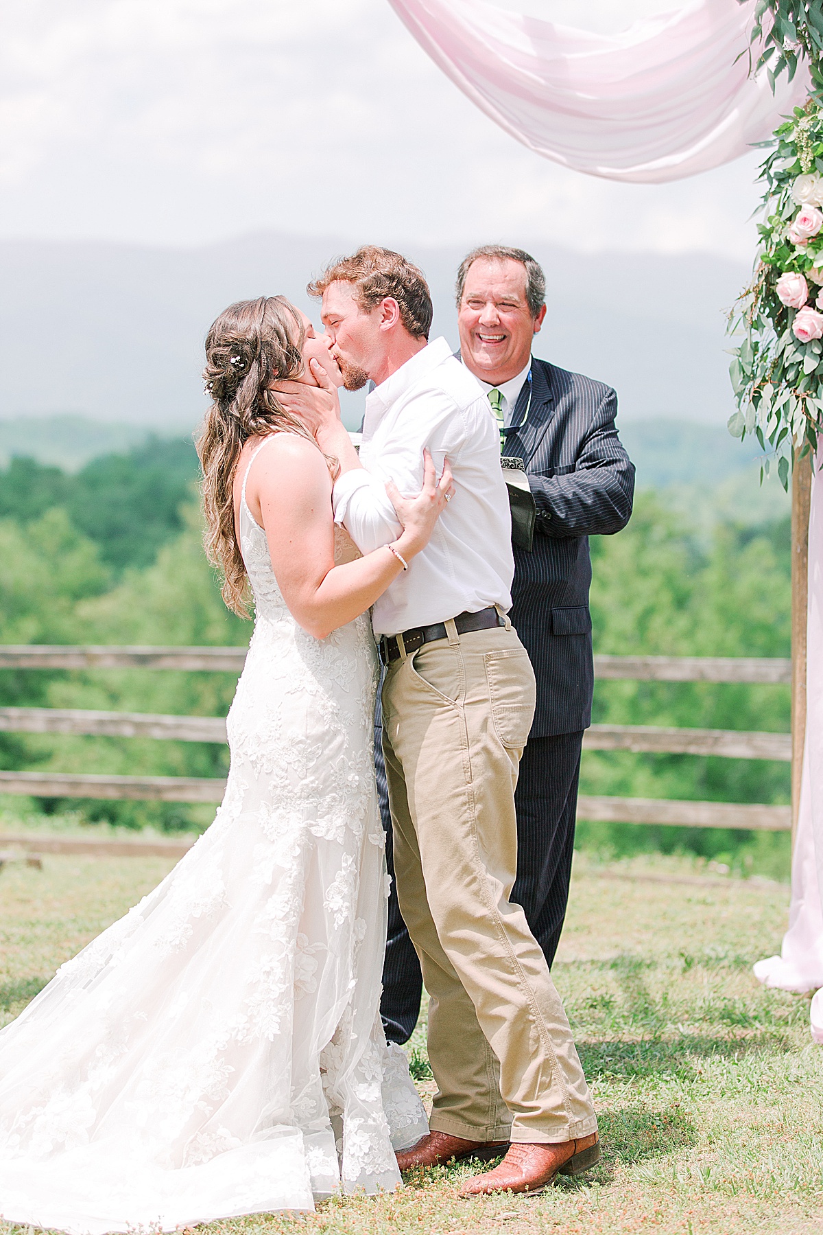 Rustic Spring Mountain Wedding Ceremony Bride and Groom's First Kiss Pastor smiling in Background Photo