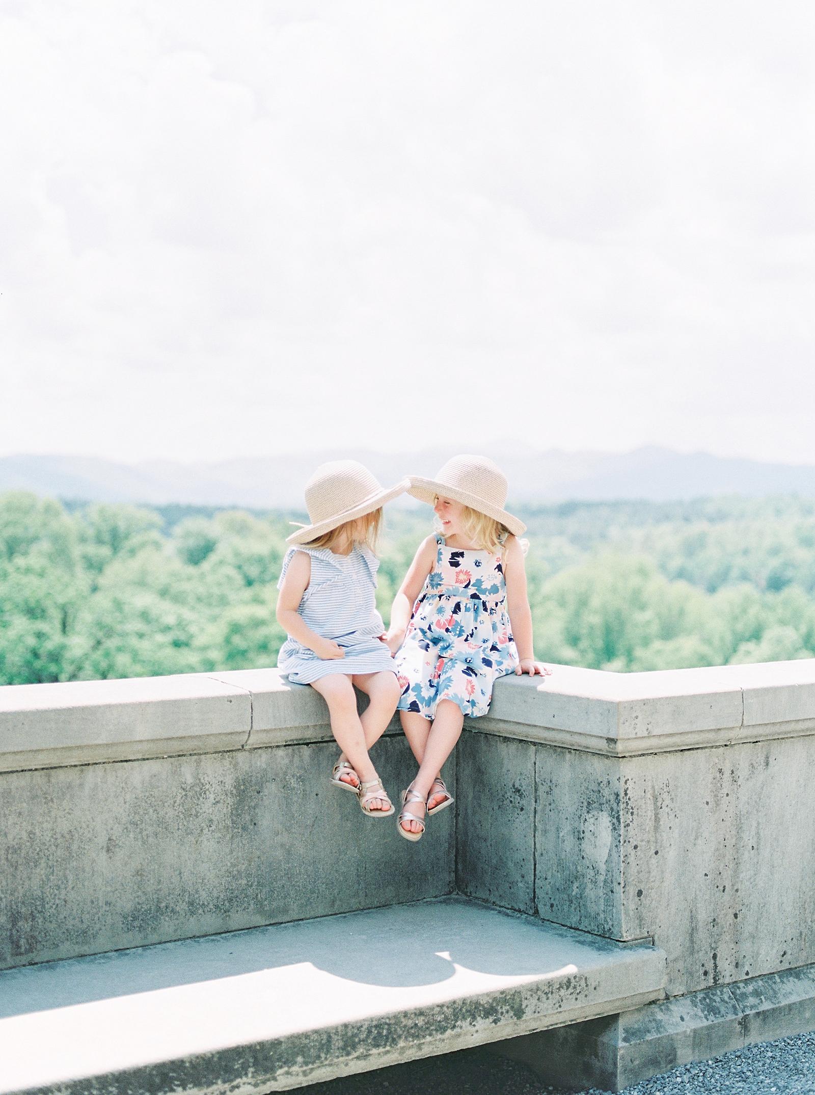 Biltmore House and Gardens Little girls sitting on wall smiling at each other with mountains in the background Photo