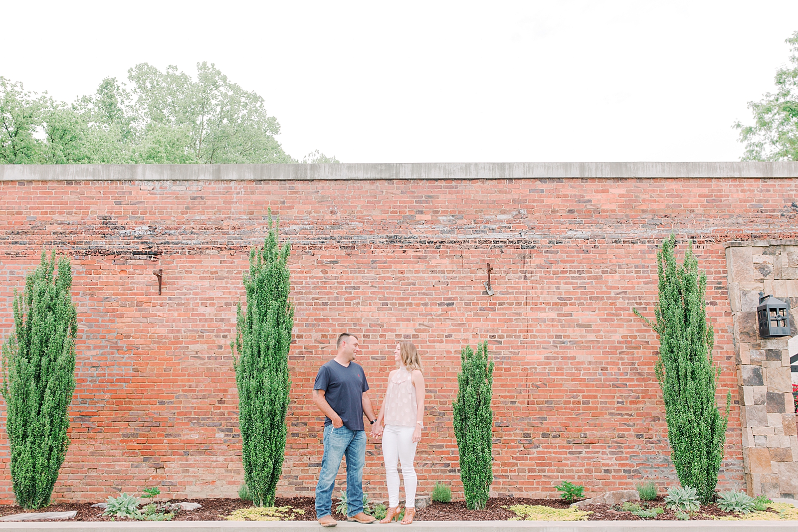 Hackney Warehouse Engagement Session couple in front of brick wall smiling at each other Photo