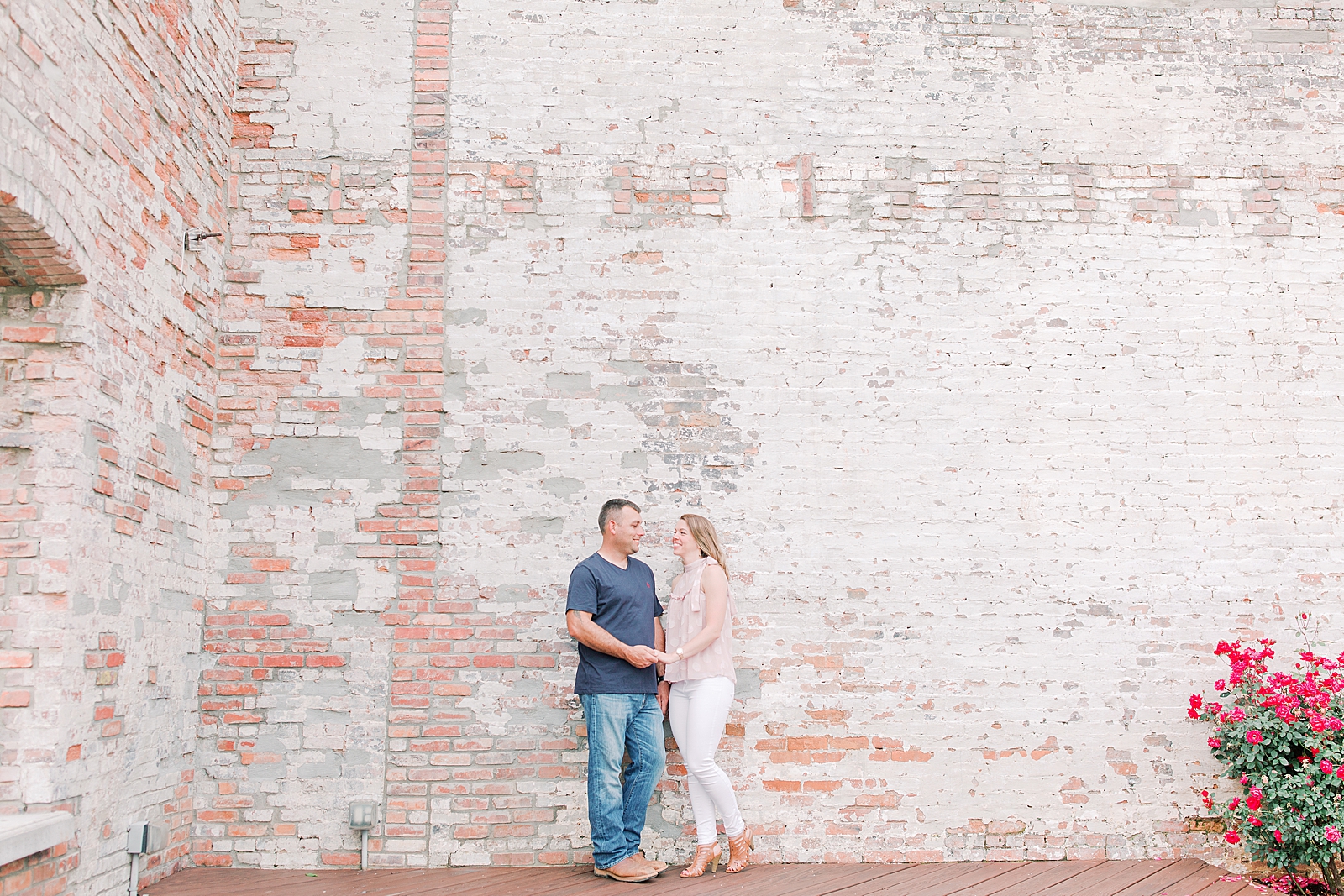 Hackney Warehouse Engagement Session couple smiling at each other in front of brick wall Photo