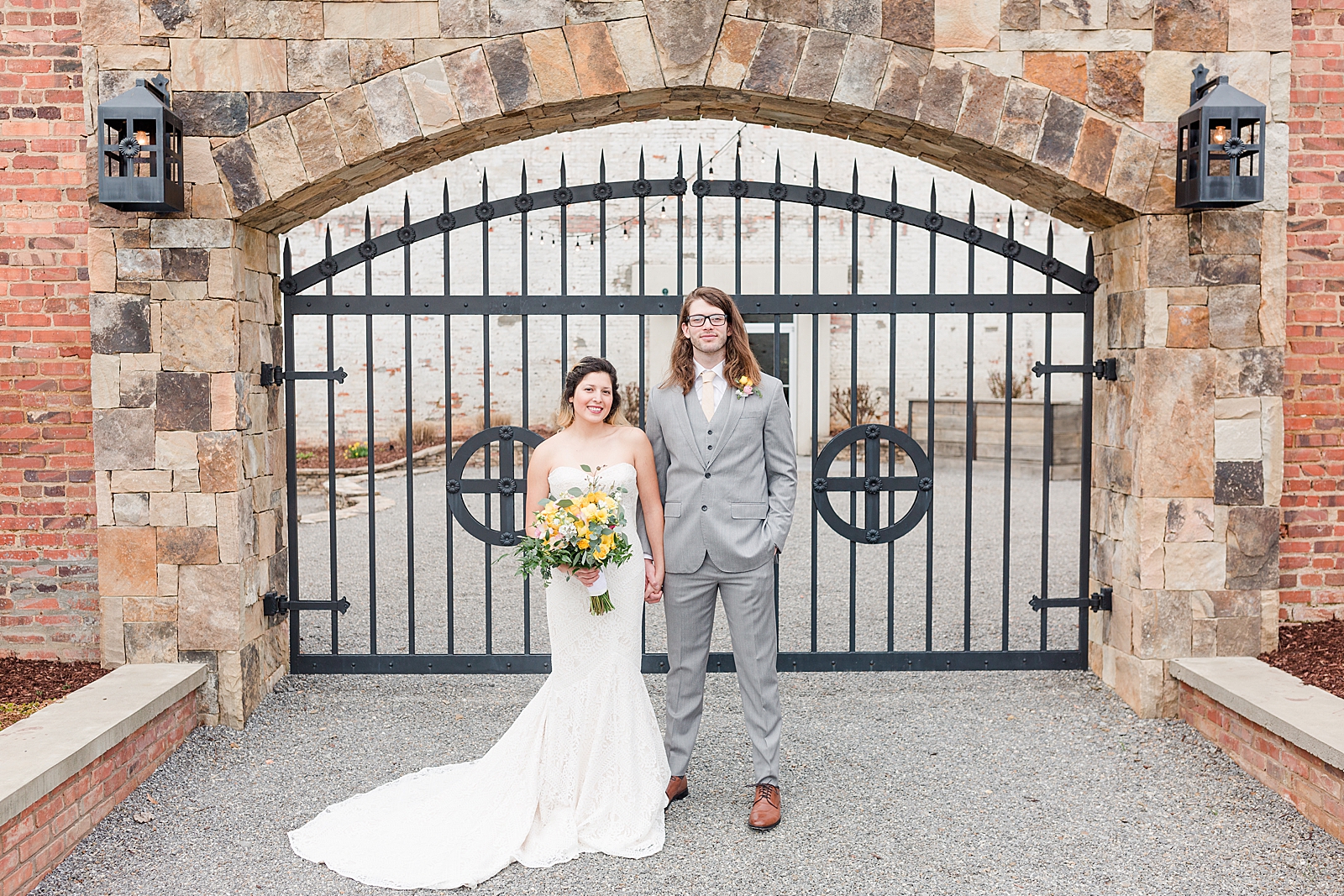 Hackney Warehouse Wedding Couple holding hands in front of Iron Gate Smiling at Camera Photo