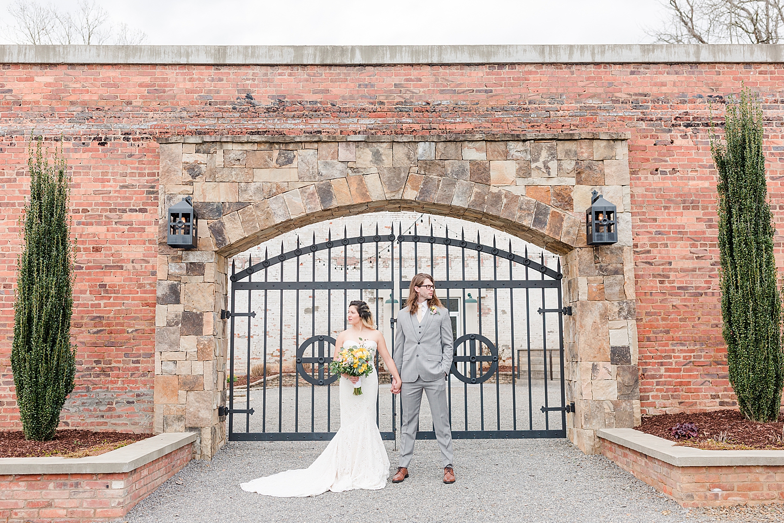 Hackney Warehouse Wedding Bride and Groom Holding Hands in Front of Iron Gate Looking the opposite ways Photo