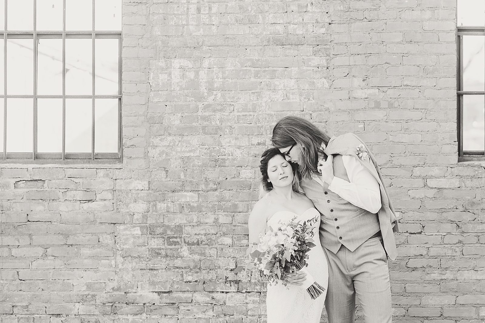 Hackney Warehouse Wedding Black and White of Groom Nuzzling Bride in Front of Brick Wall Photo
