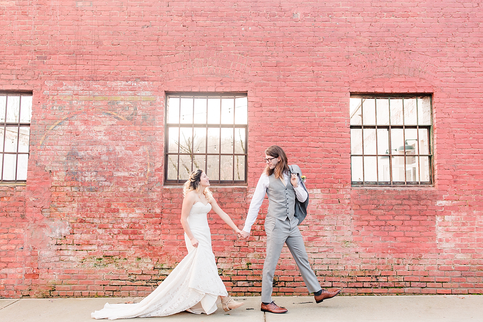 Hackney Warehouse Wedding Bride and Groom Walking in front of Brick wall holding hands Photo