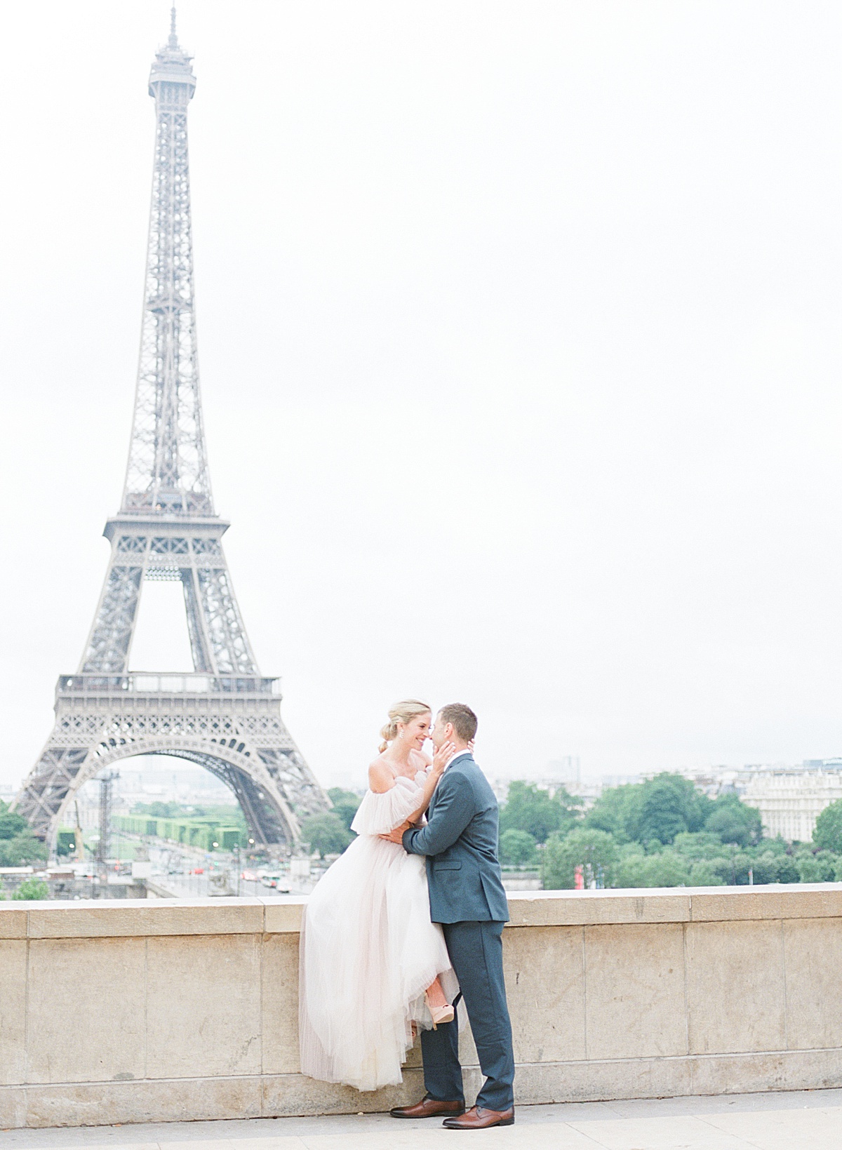 Eiffel Tower Wedding Bride Sitting on Wall Snuggling Groom Photo