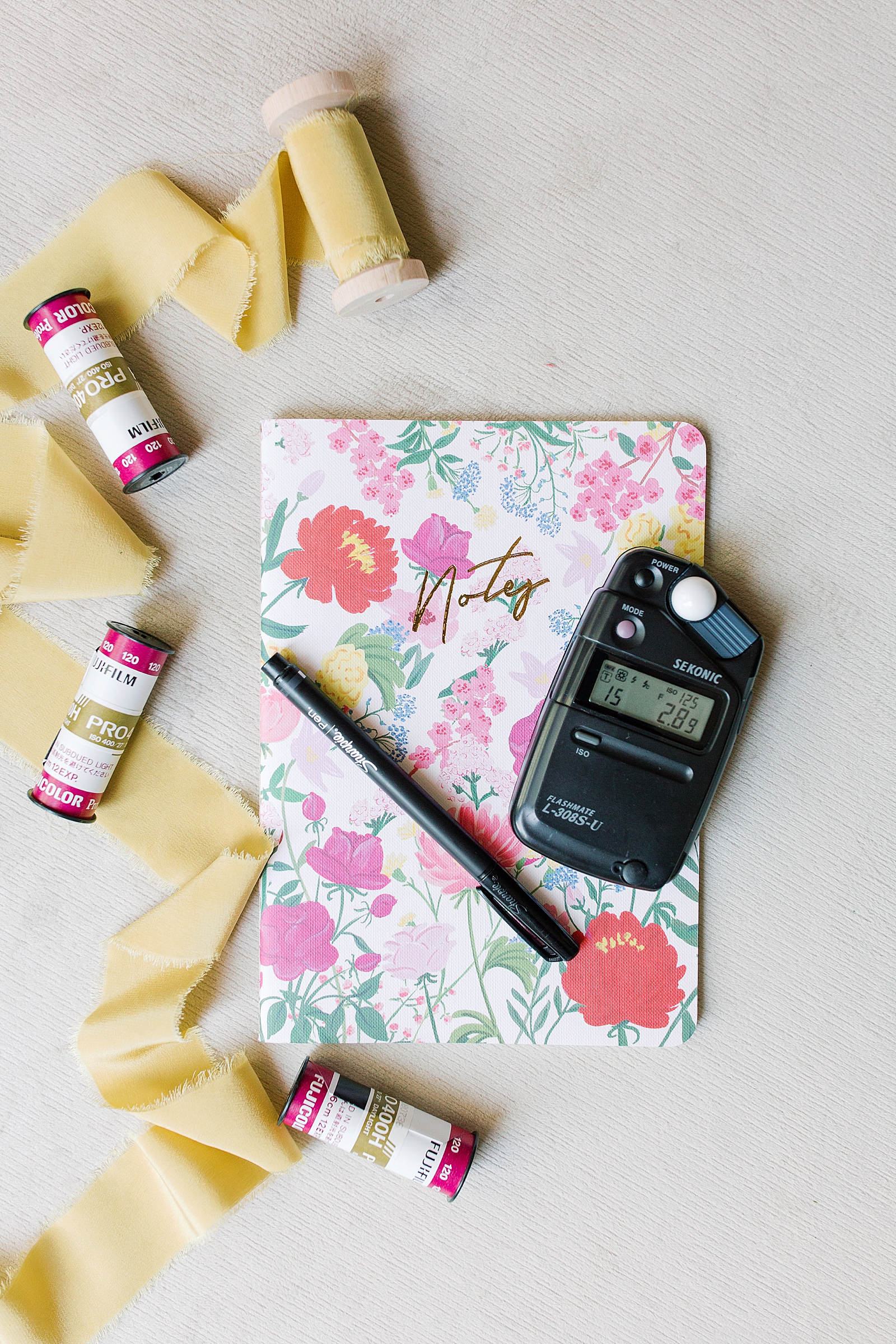 A flat lay image of whats in my camera bag including rolls of film a light meter and notebook with pen photo