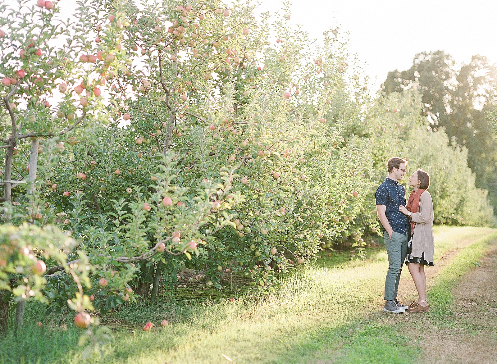 Downtown Asheville Engagement Session Couple Smiling at Each Other Standing in Orchard Photo