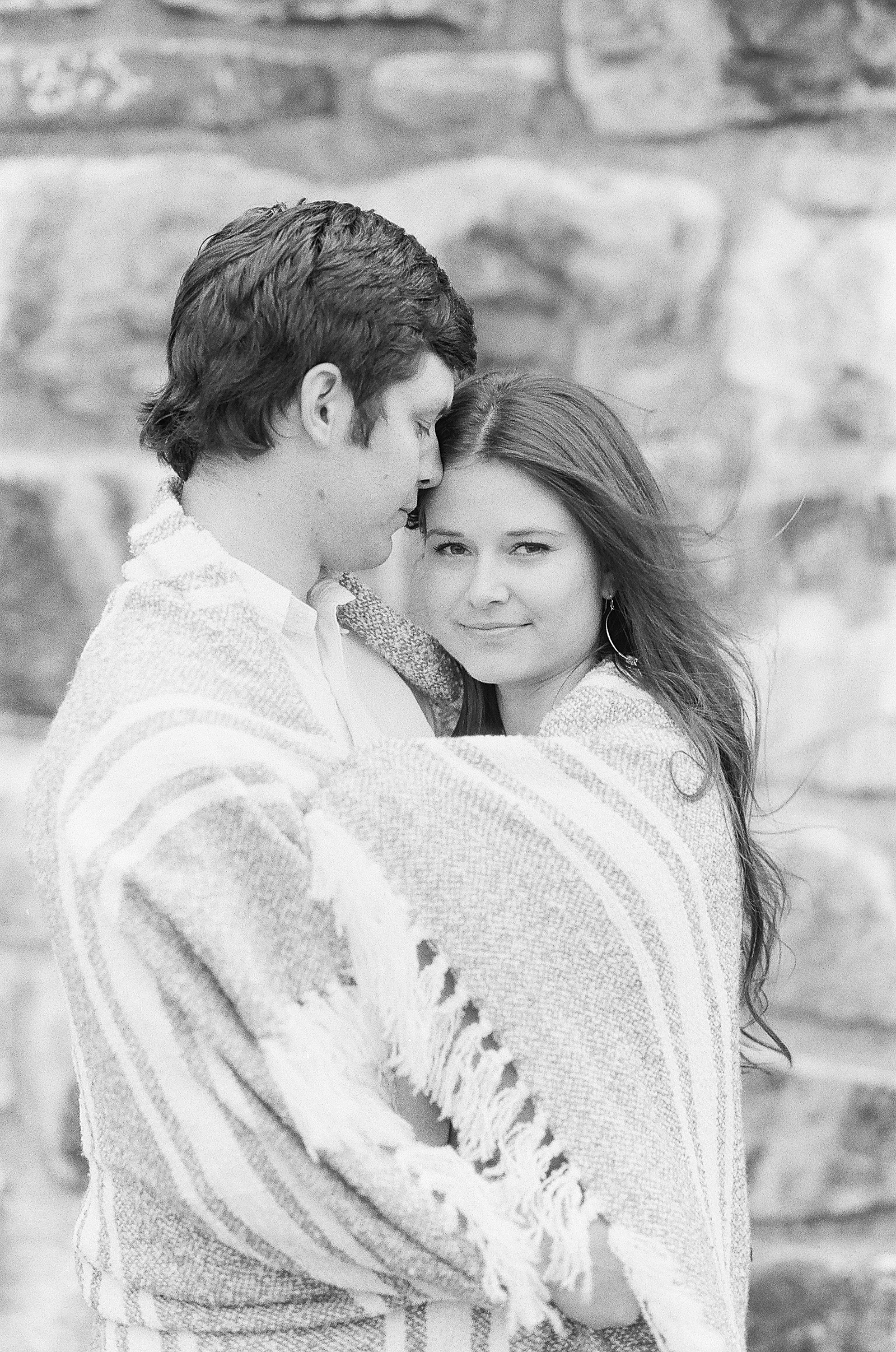 Mountaintop Engagement Black and White of Couple hugging Sierra looking at camera wrapped in blanket Photo 