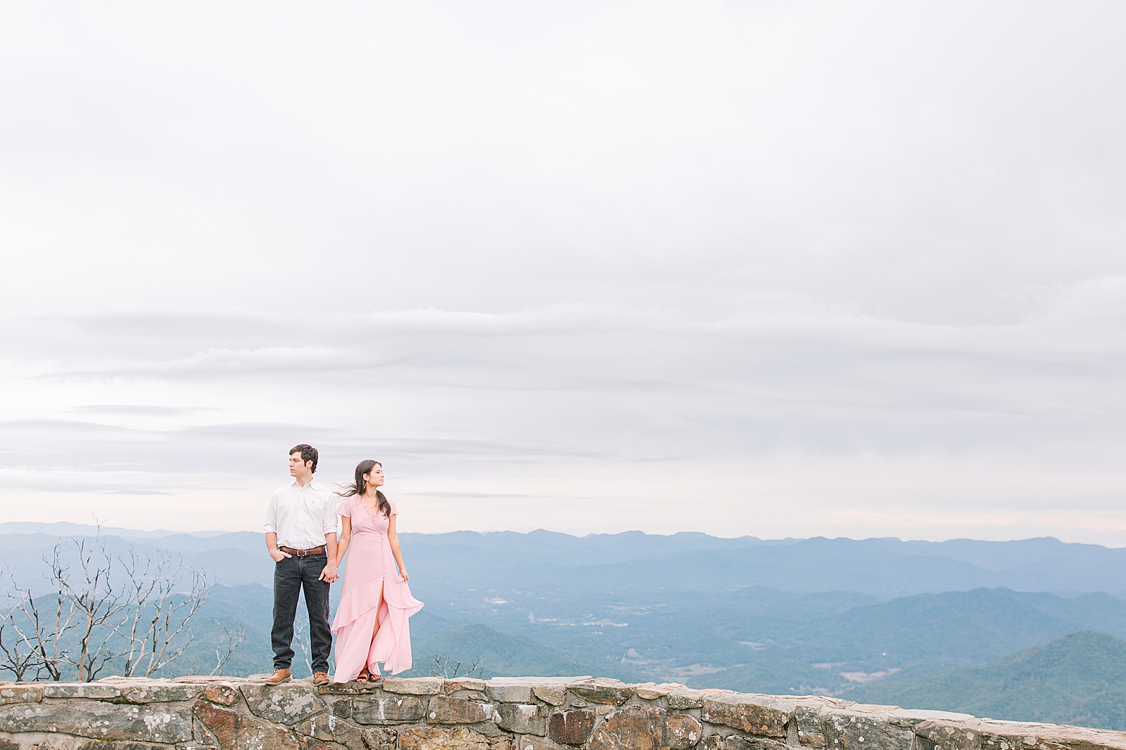 Mountaintop Engagement Couple Looking off holding hands on wall Photo 