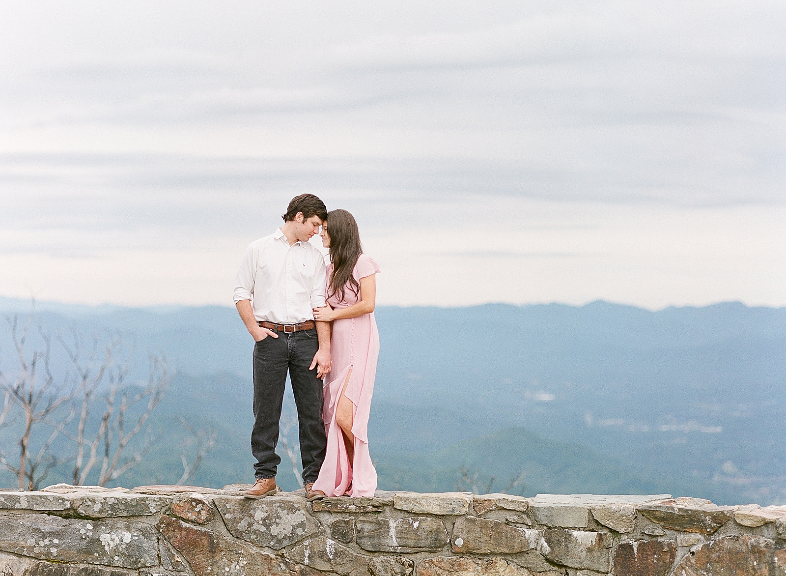 Mountaintop Engagement Couple nose to nose hugging on wall with mountains in background Photo 