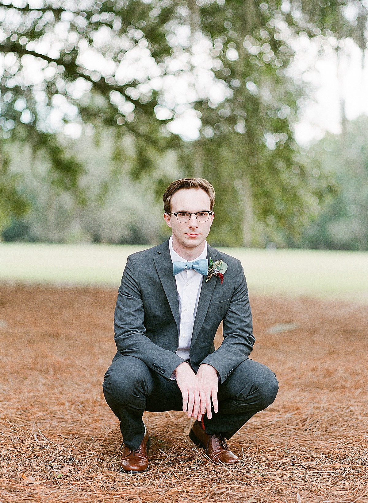 Groom Michael Squatting Looking at Camera Under Trees Photo 