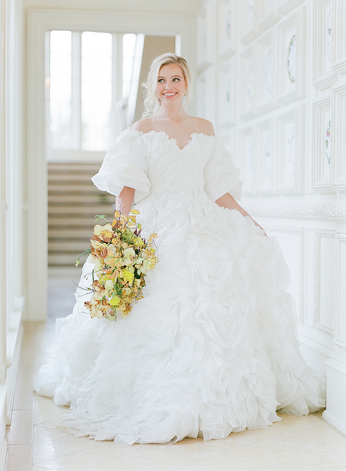 Bride walking down Hall at Olana Wedding Venues in Dallas Holding Yellow Bouquet Photo