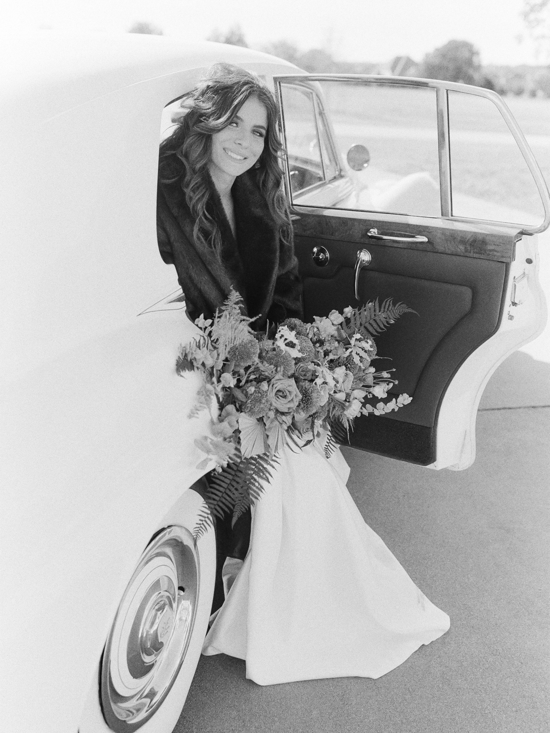 Black and White of Bride sitting in Car holding Bouquet Smiling at camera Photo 