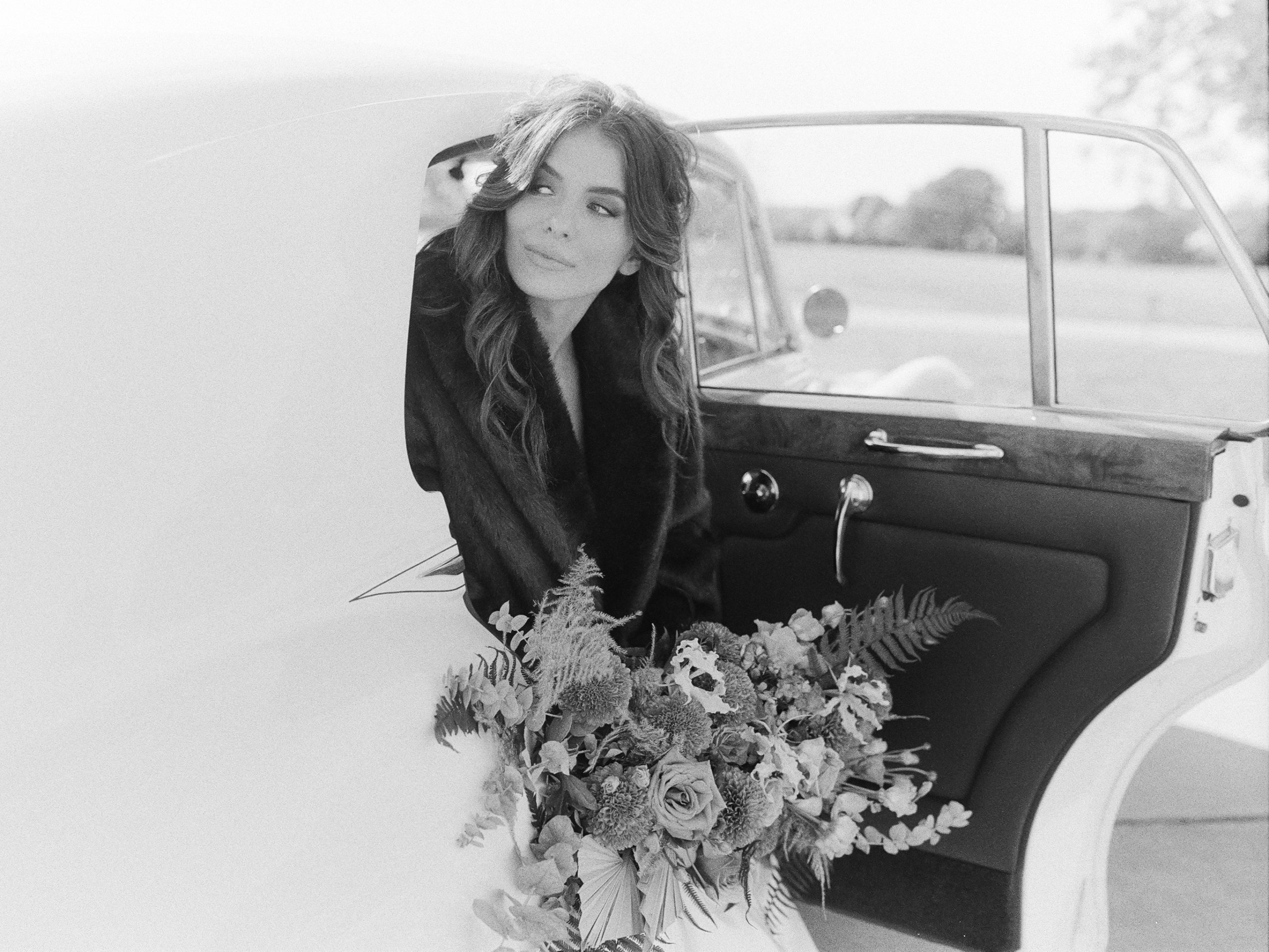 Black and White of Bride Sitting in Rolls Royce Looking off 