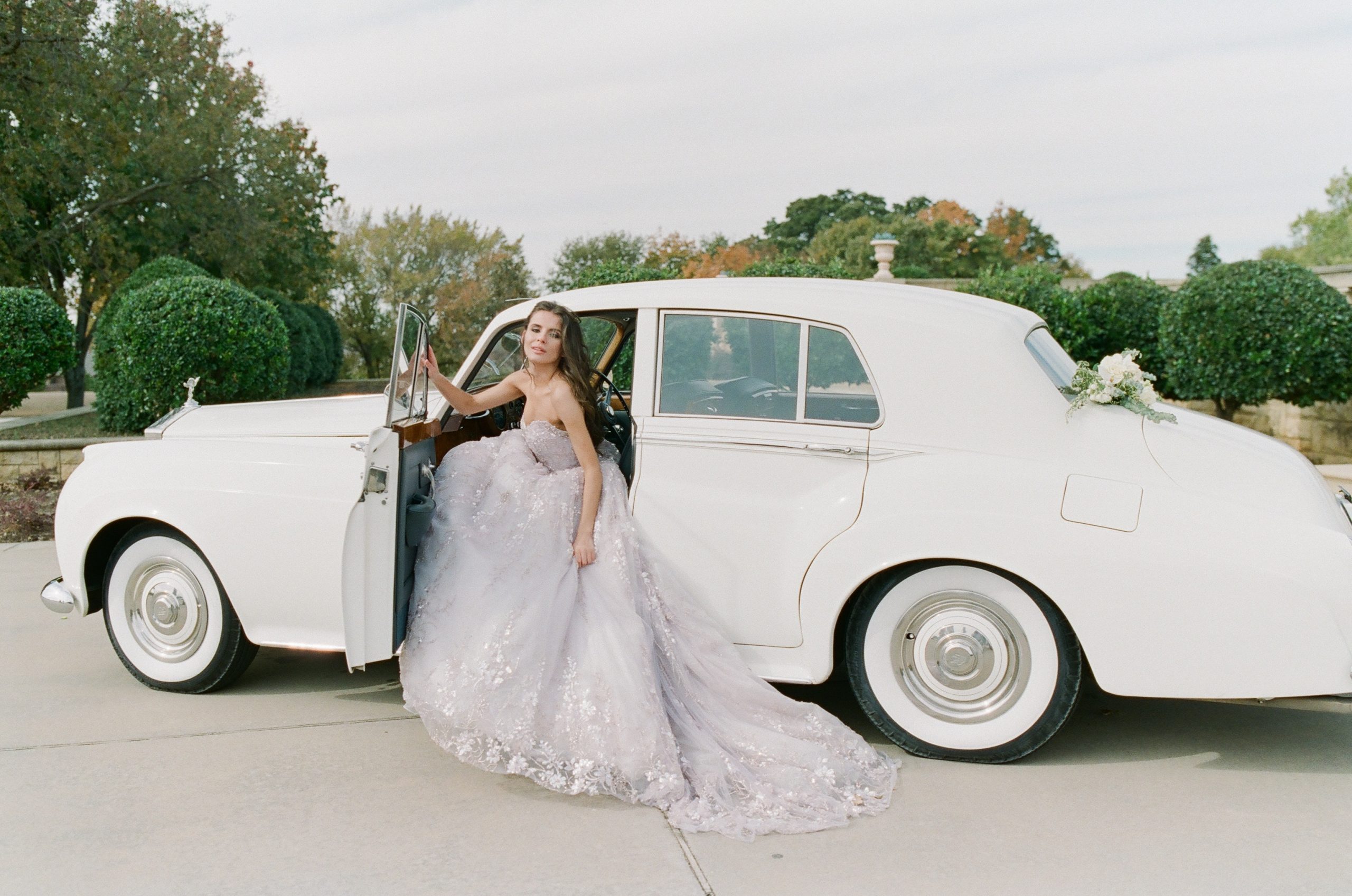 Bride in Lavender Couture Wedding Dress Sitting in Vintage Car Photo