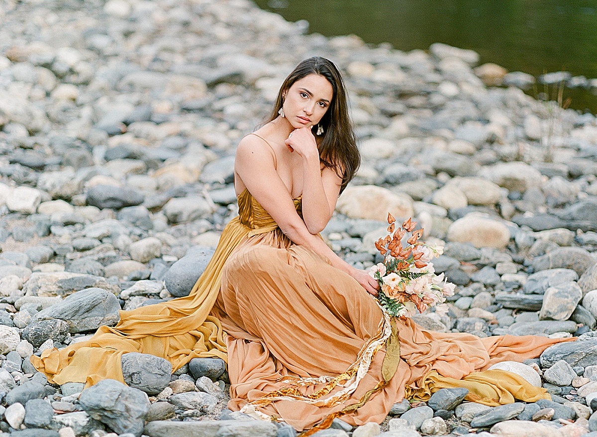 Leanne Marshall Golden Gown Model Sitting On Rocks Holding Bouquet Photo