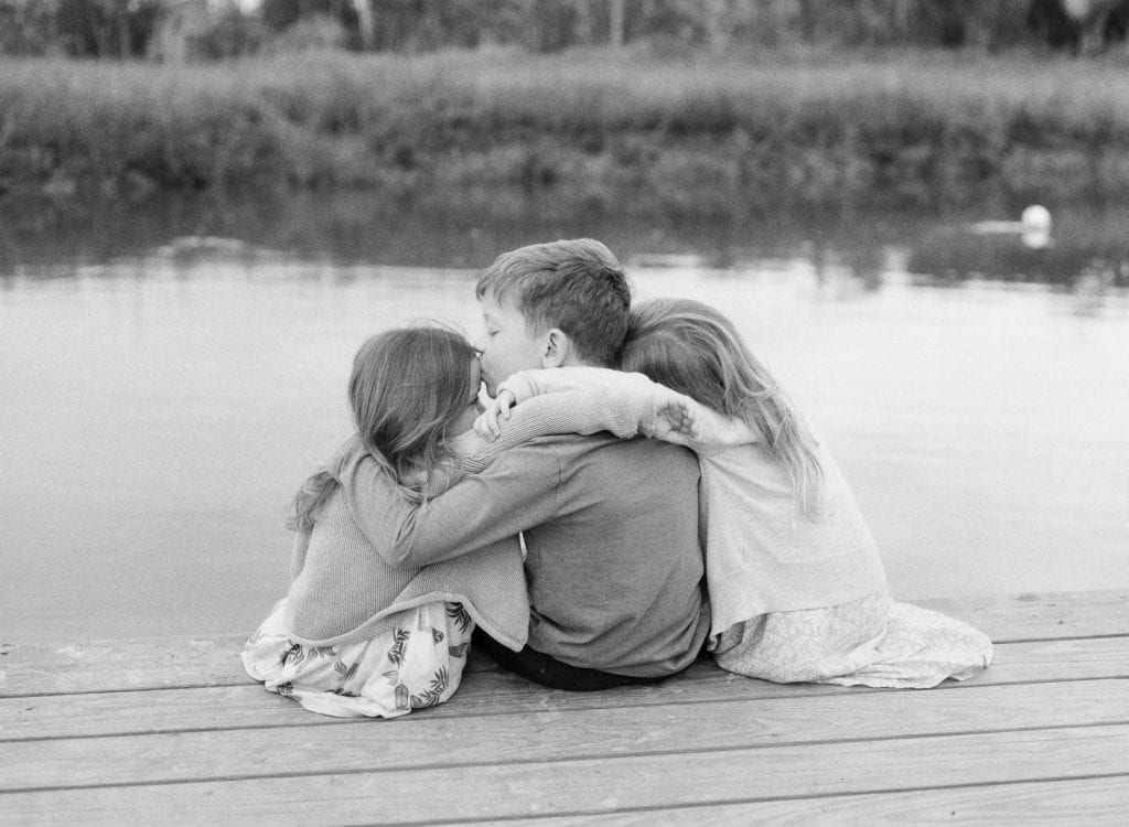 Black and White of three kids sitting on a dock, brother with two sisters photo