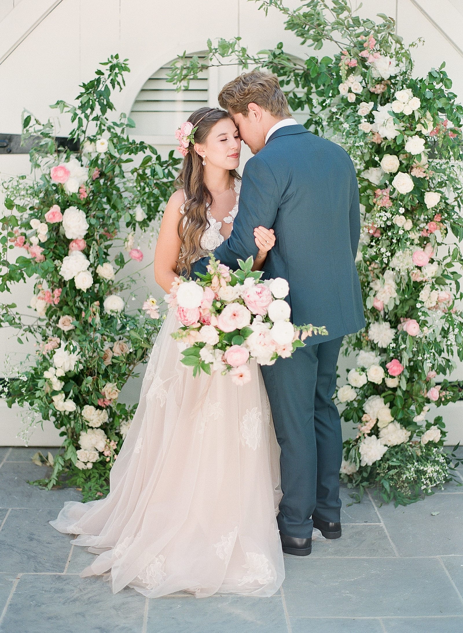 Bride and Groom Snuggled together in Front of Floral Ceremony Arch Photo 