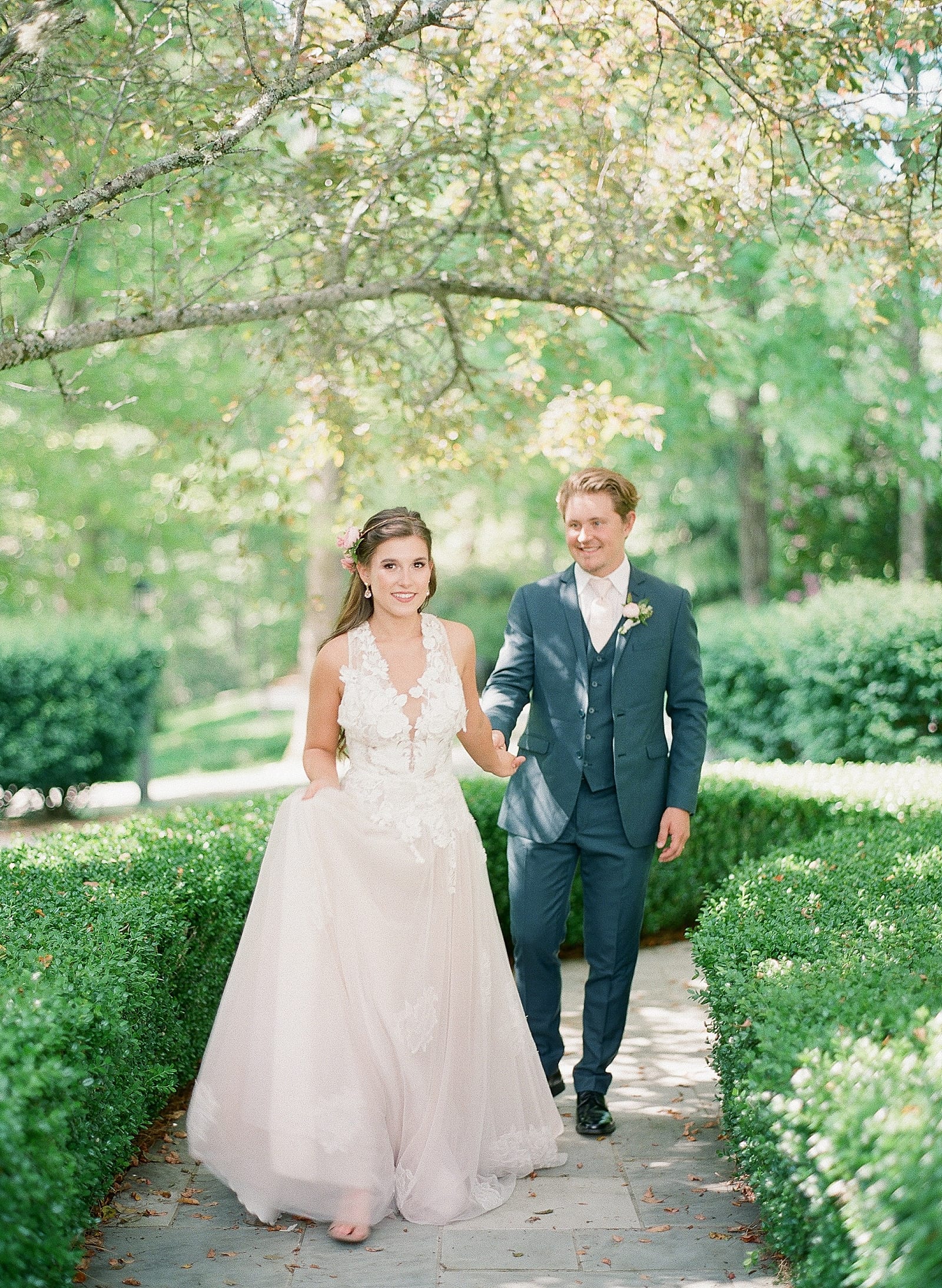 Bride and Groom Holding Hands Walking toward Camera on Path Photo 