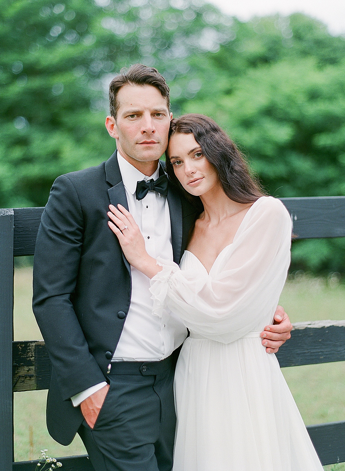 Bride and Groom Leaning against black fence looking at Camera