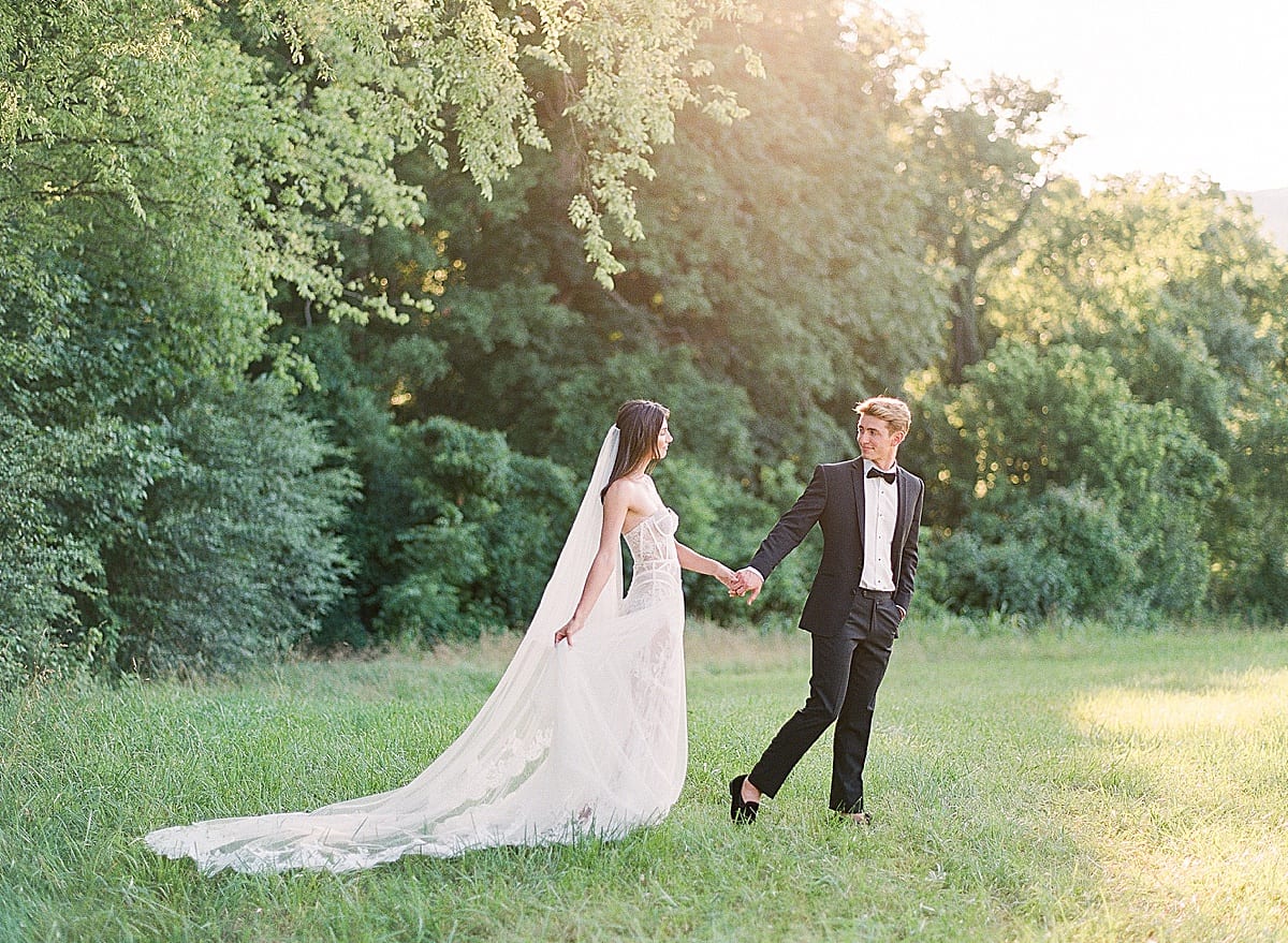 Bride and Groom Holding Hands Walking Through Grass Photo 