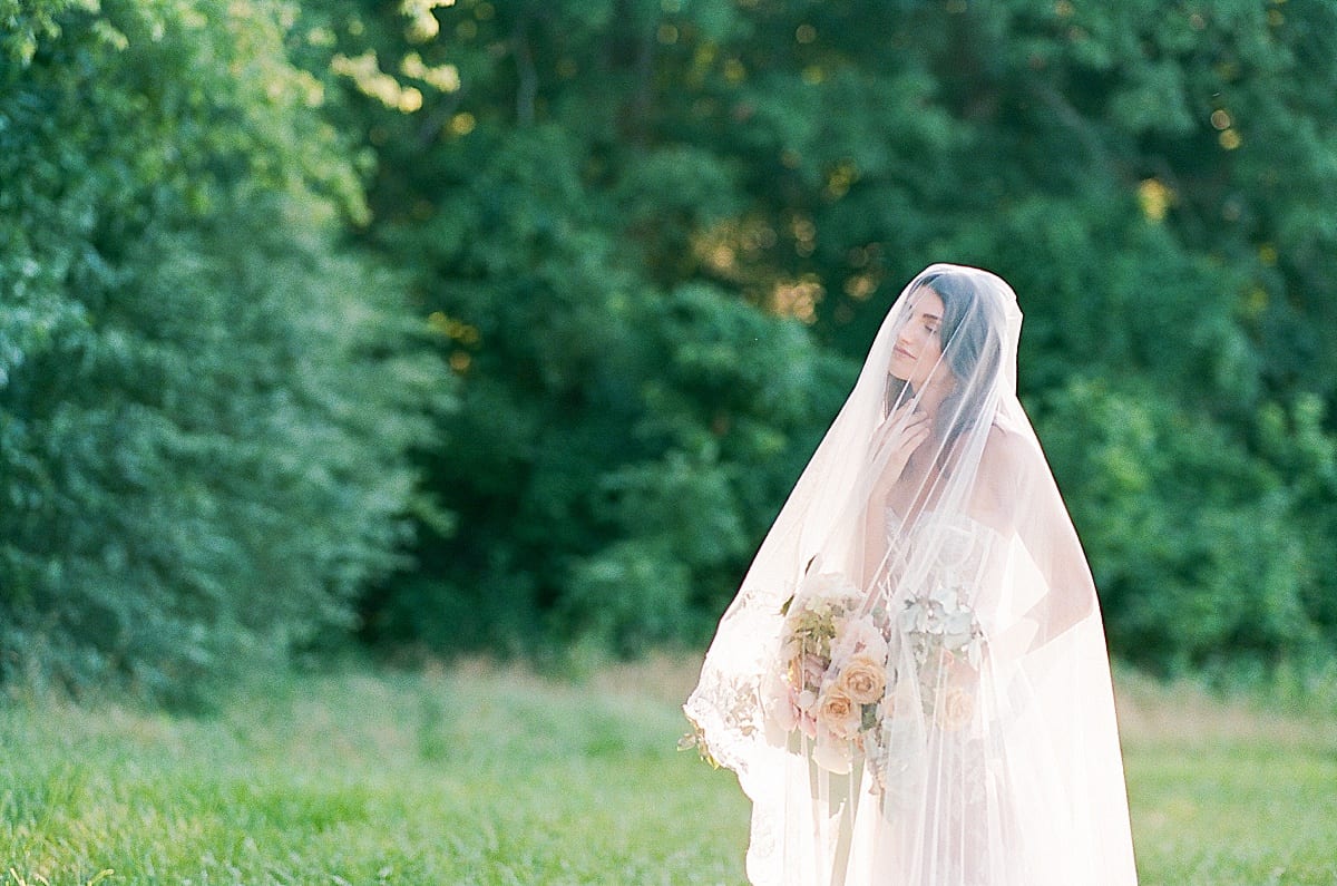 Bride with hand under chin holding bouquet and veil over her