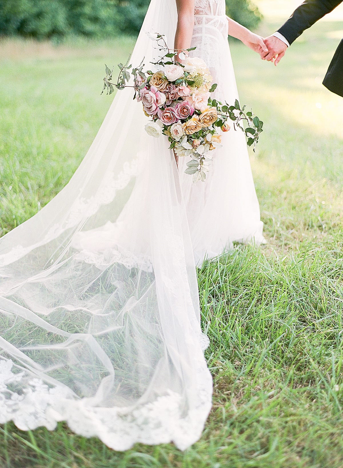 Bridal Bouquet with veil trailing behind and Bride holding grooms hand 