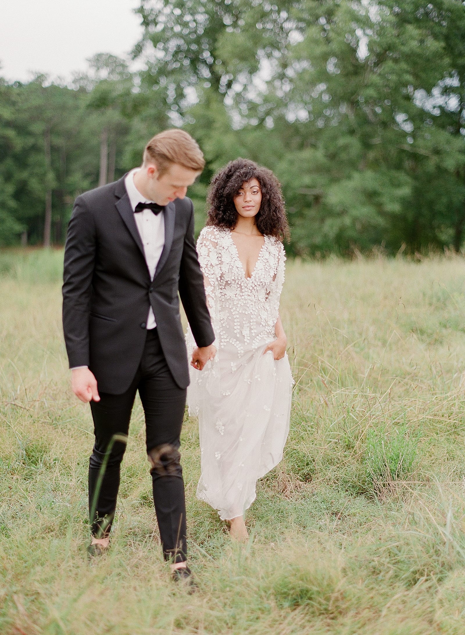 Bride and Groom Walking Through Field Holding Hands Photo