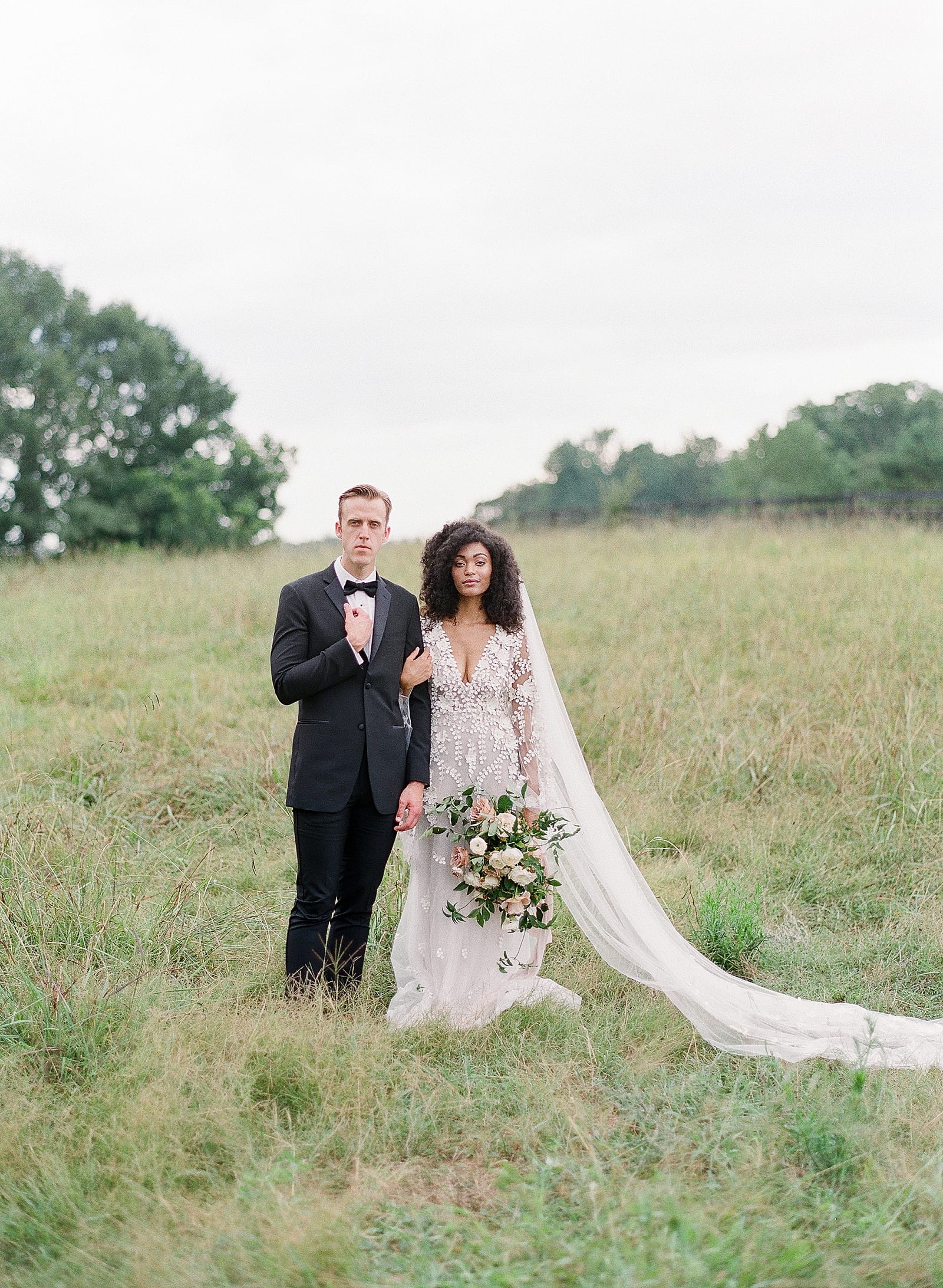 Bride and Groom Linking Arms In Field Looking at Camera Photo