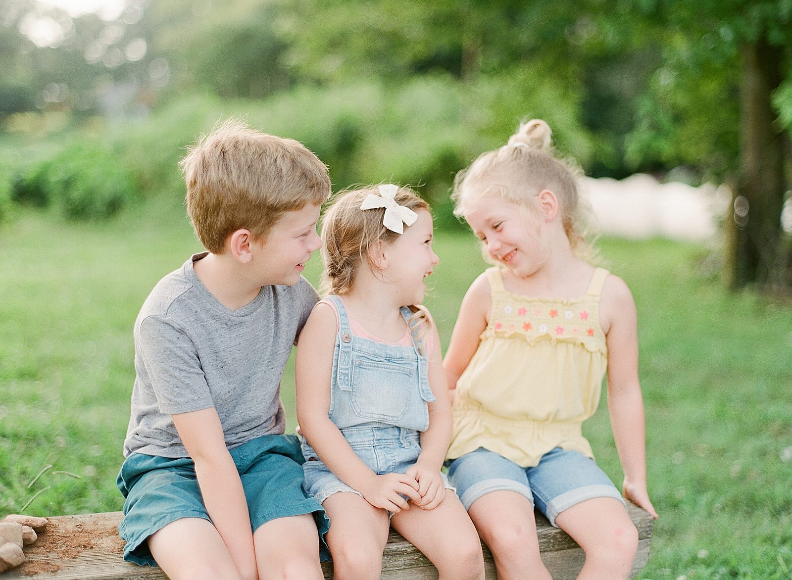Brother and Two Sisters Sitting On Bench Laughing Photo