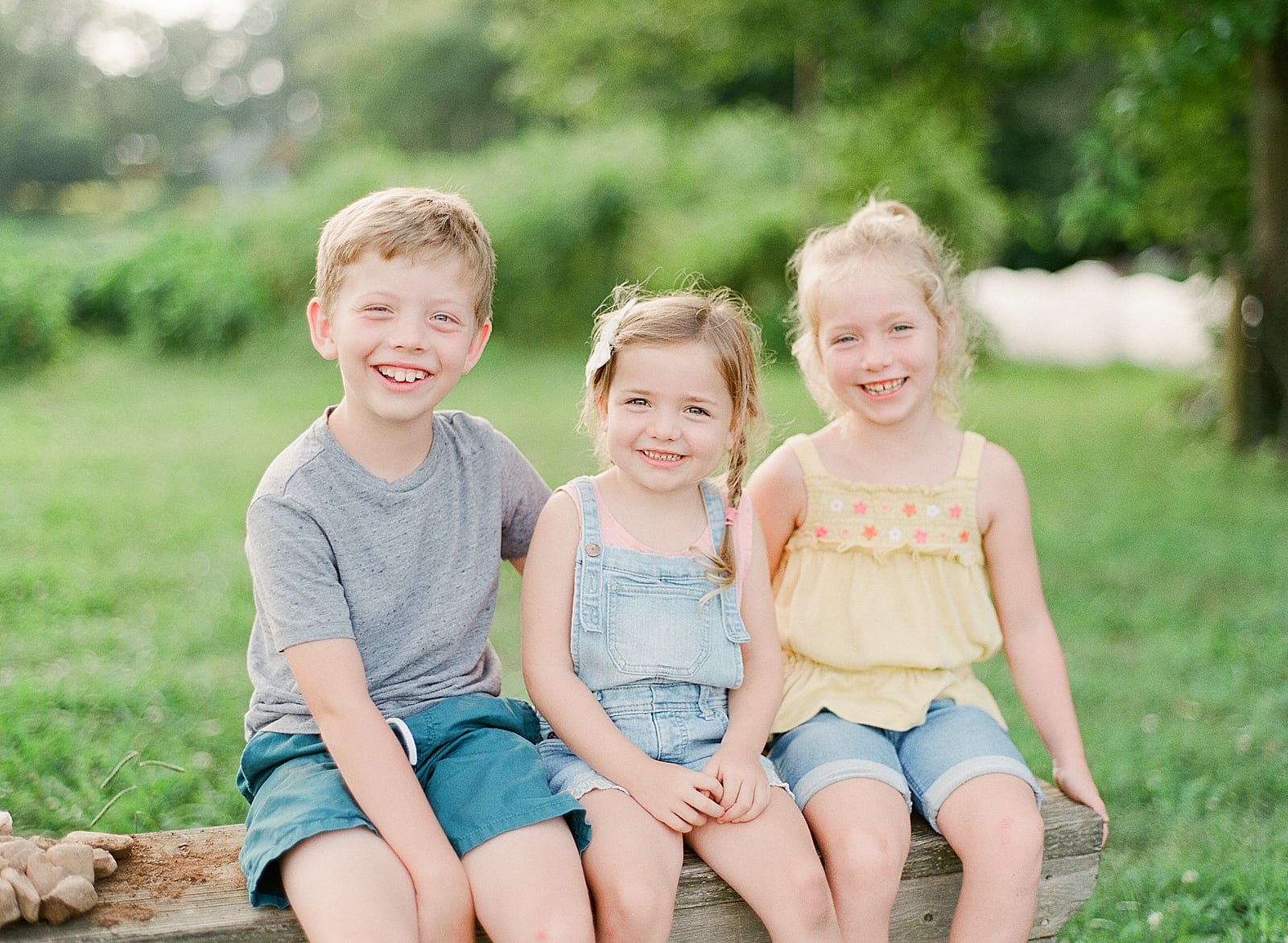 Brother and Two Sisters Smiling at Camera on Bench Photo