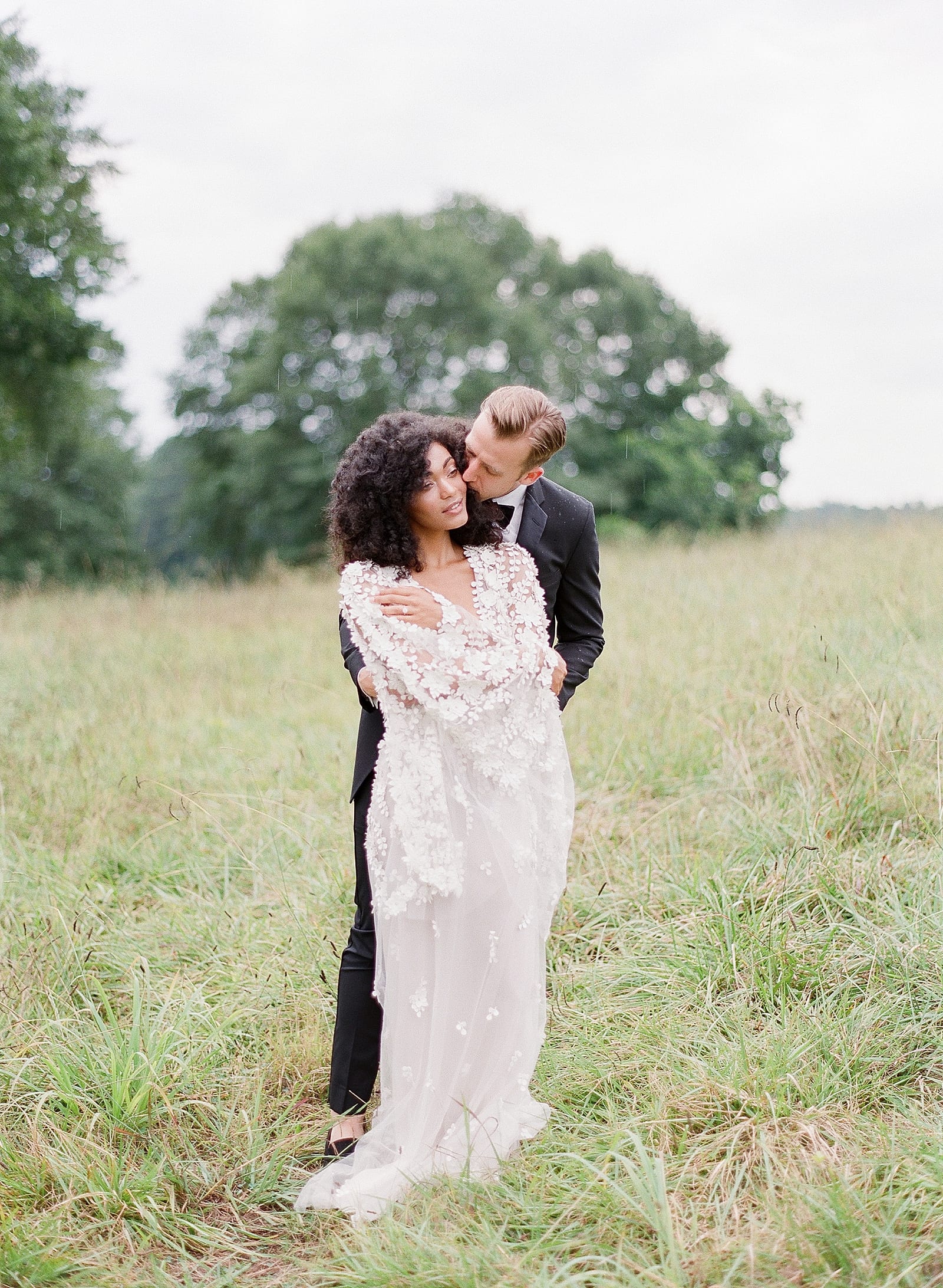 Groom Hugging and Kissing Bride in Field Photo
