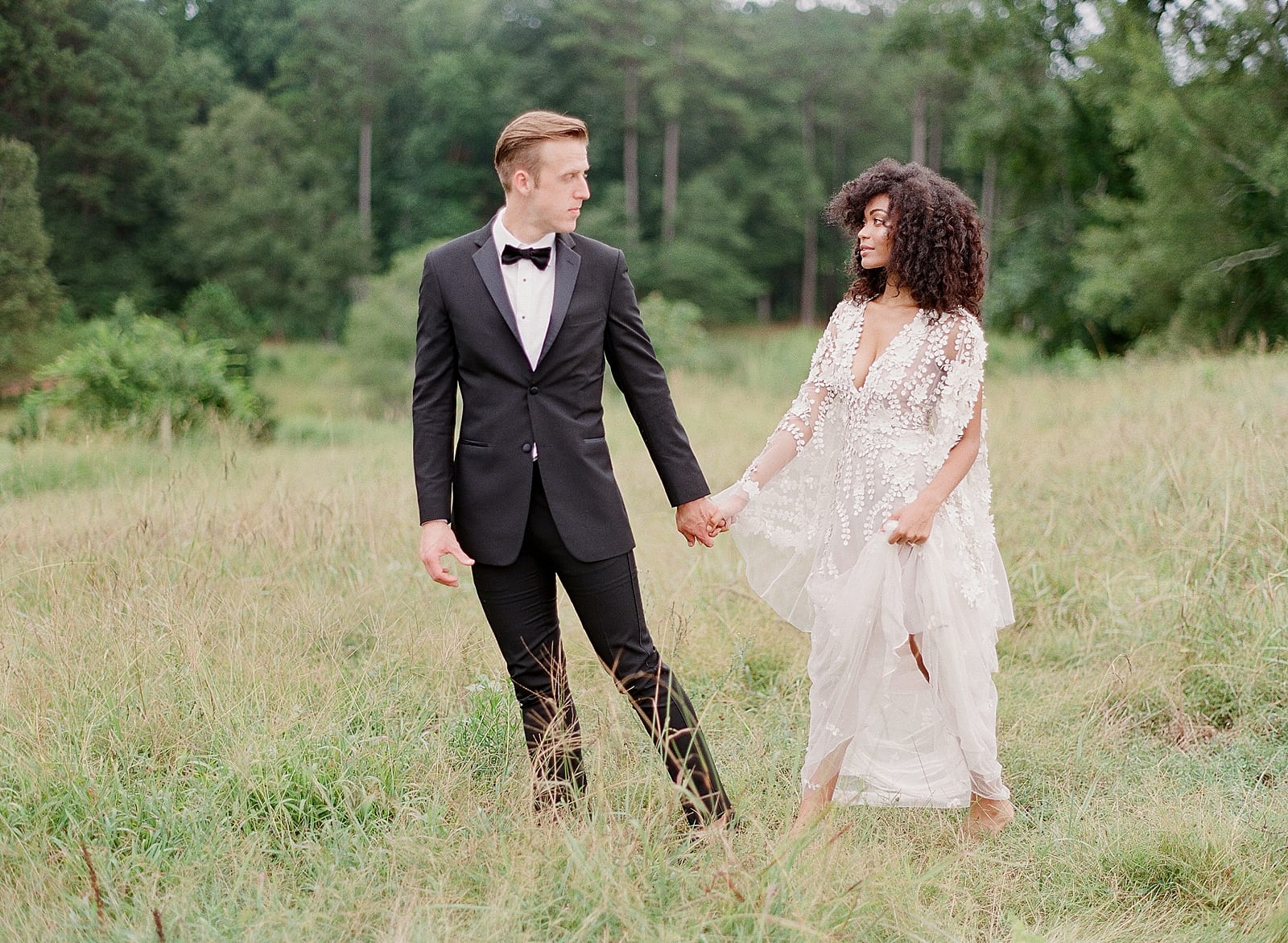 Bride and Groom Holding Hands Walking Through Field Photo