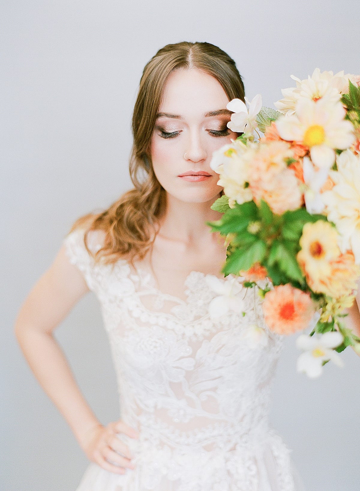 Bride with Wedding Hair and Makeup Holding Bouquet in Front of Face Looking Down Photo