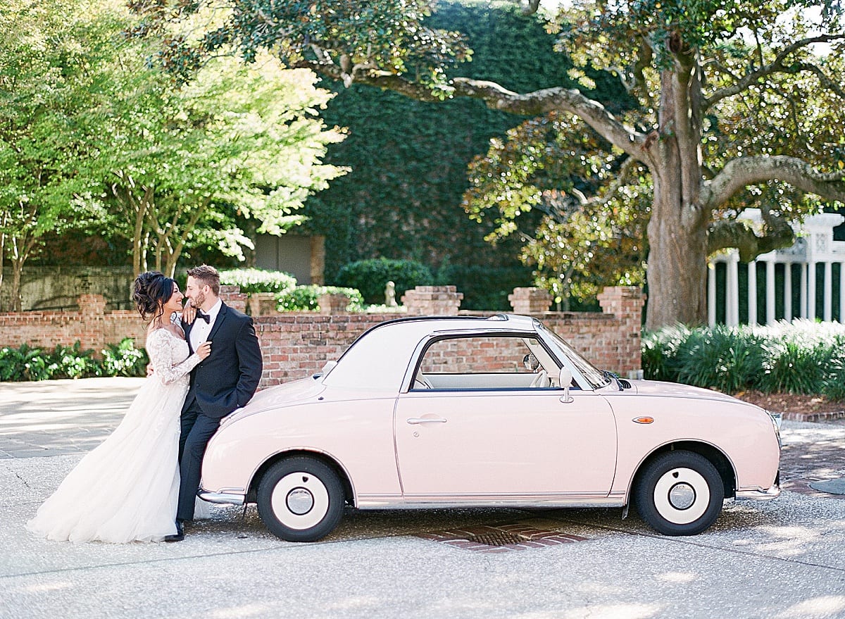 Bride and Groom Smiling at Each Other Leaning on Pink Car Photo